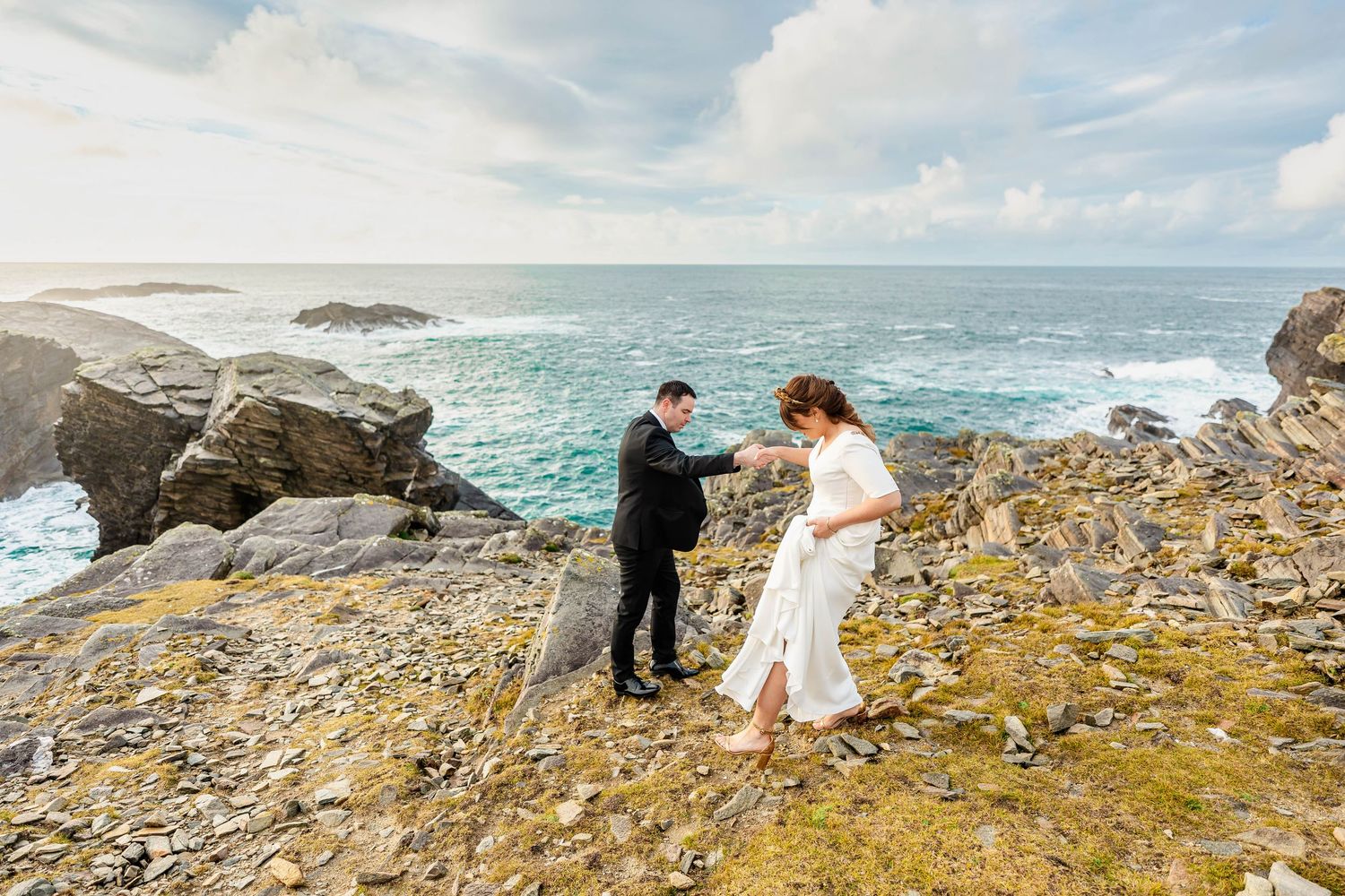 Couple taking wedding photos on dramatic rocky coastal cliffs overlooking the ocean on a cloudy day.