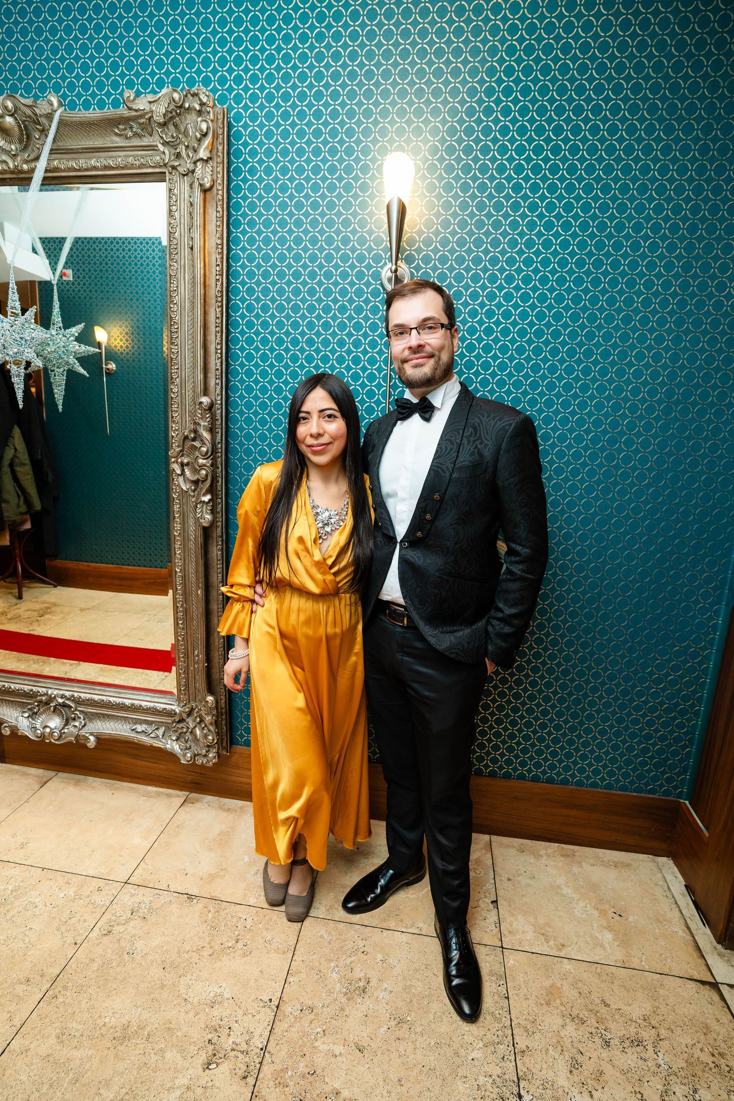 Formal portrait against turquoise patterned wallpaper in elegant venue setting.