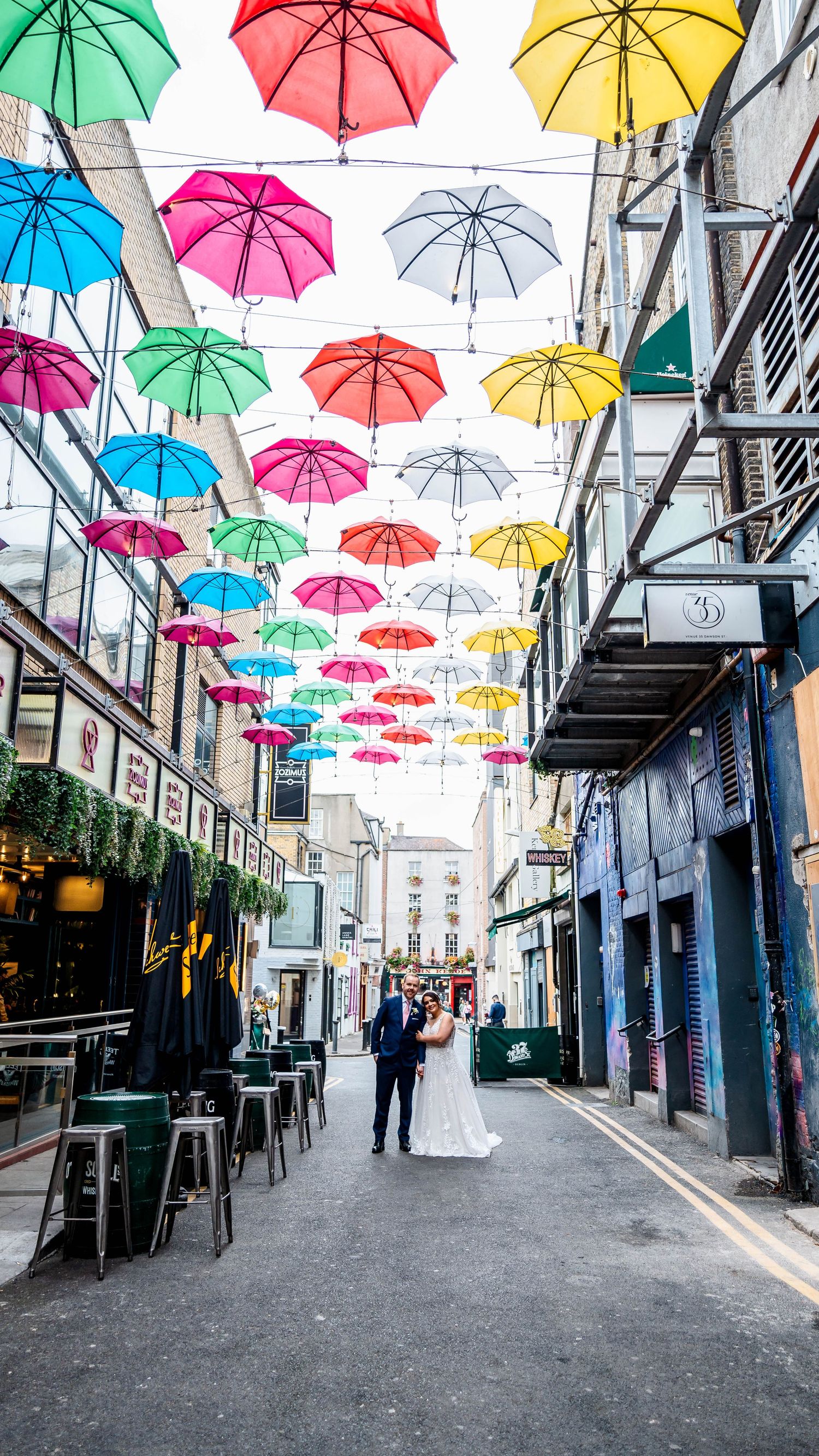Multicolored umbrella art installation hanging above urban alleyway.