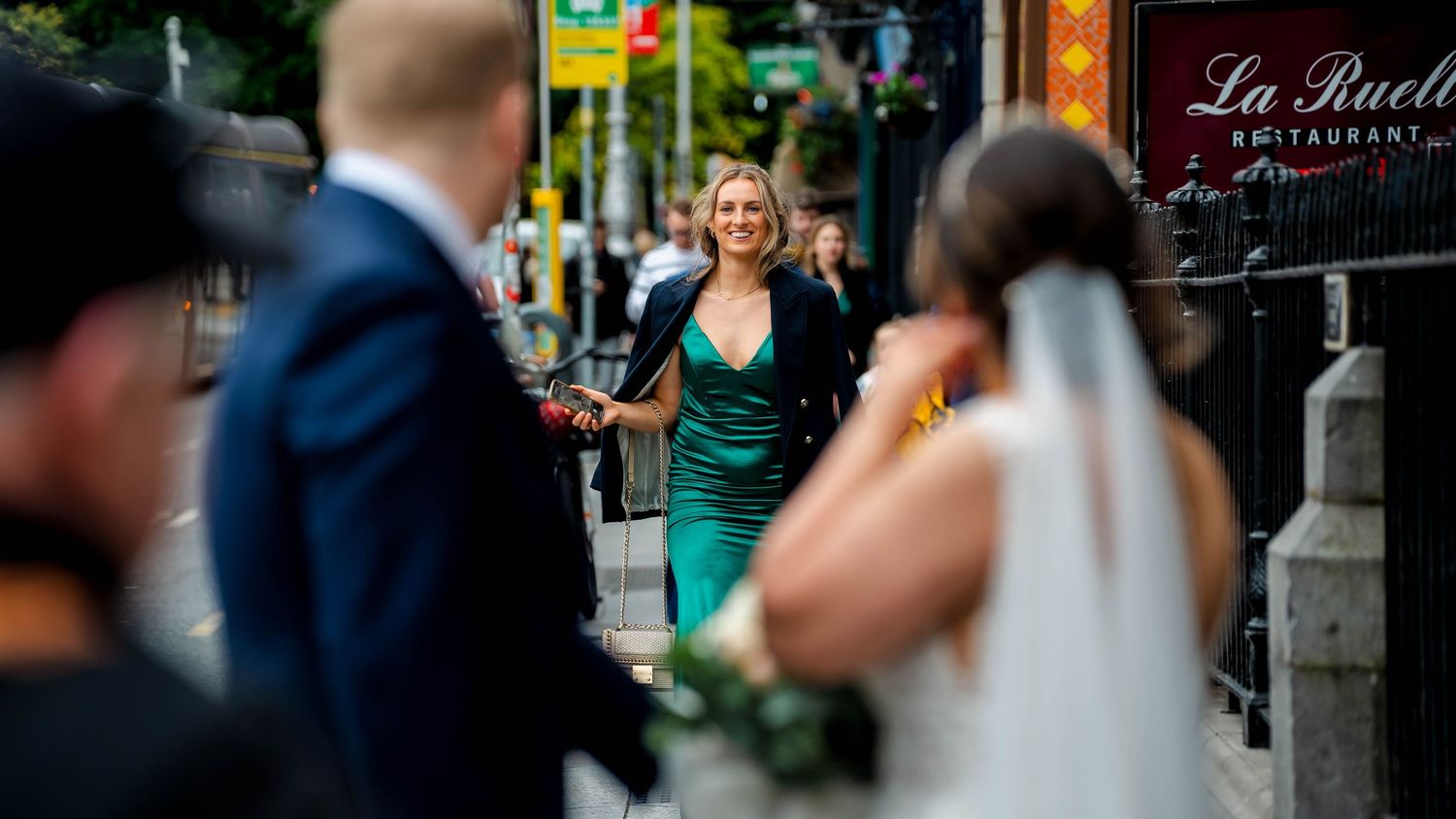 Urban street scene with storefronts and wedding celebration in soft focus.