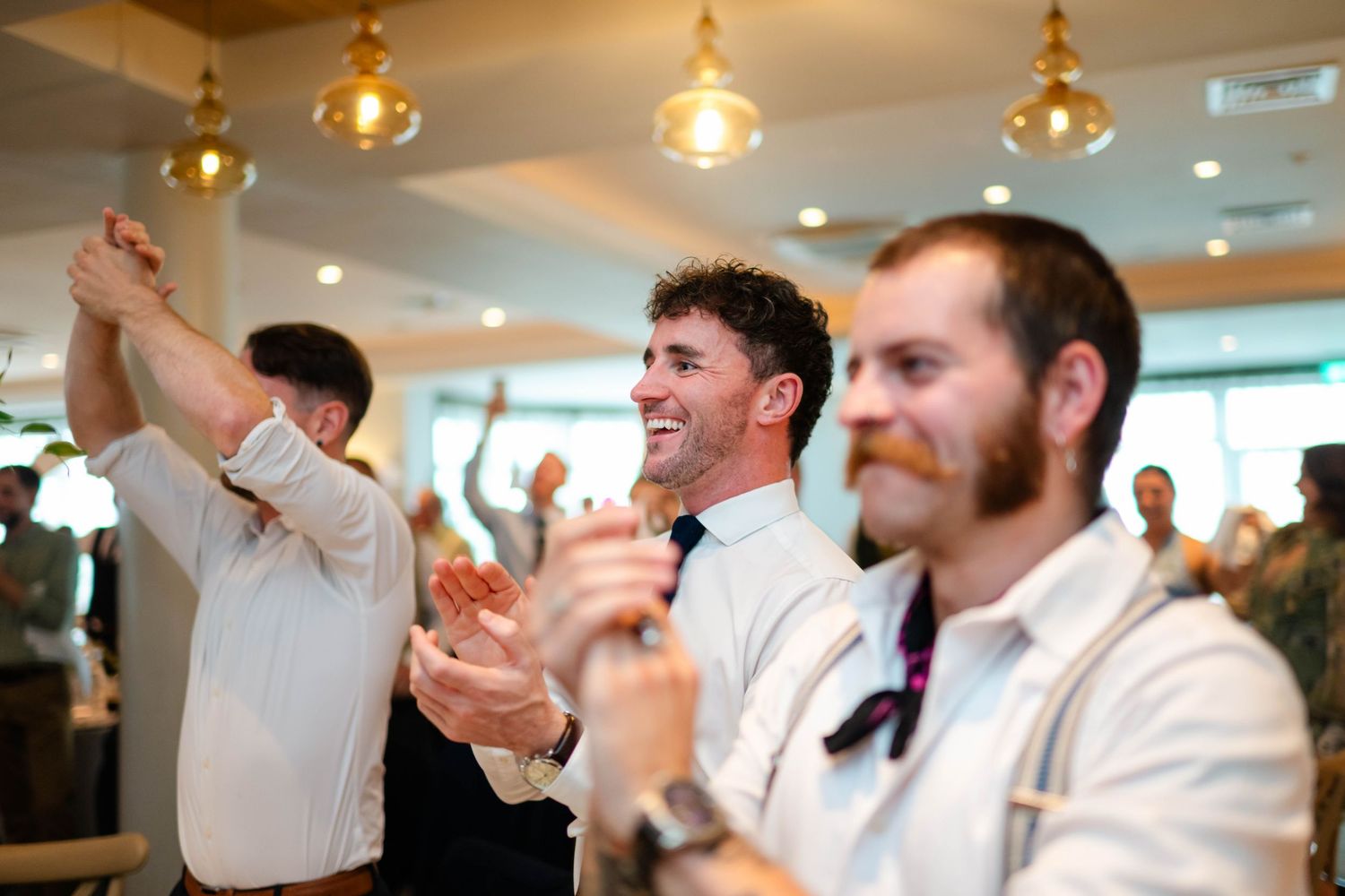 Guests cheering and raising their hands during a lively wedding reception celebration.