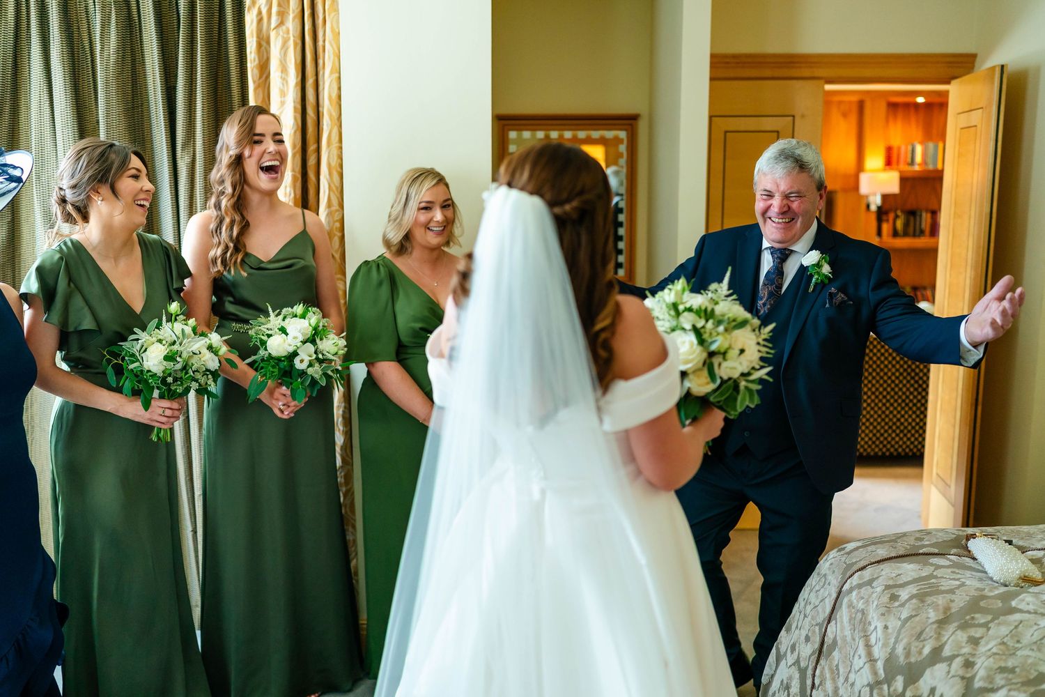 Wedding party members line up in a hotel corridor with green dresses and formal attire.