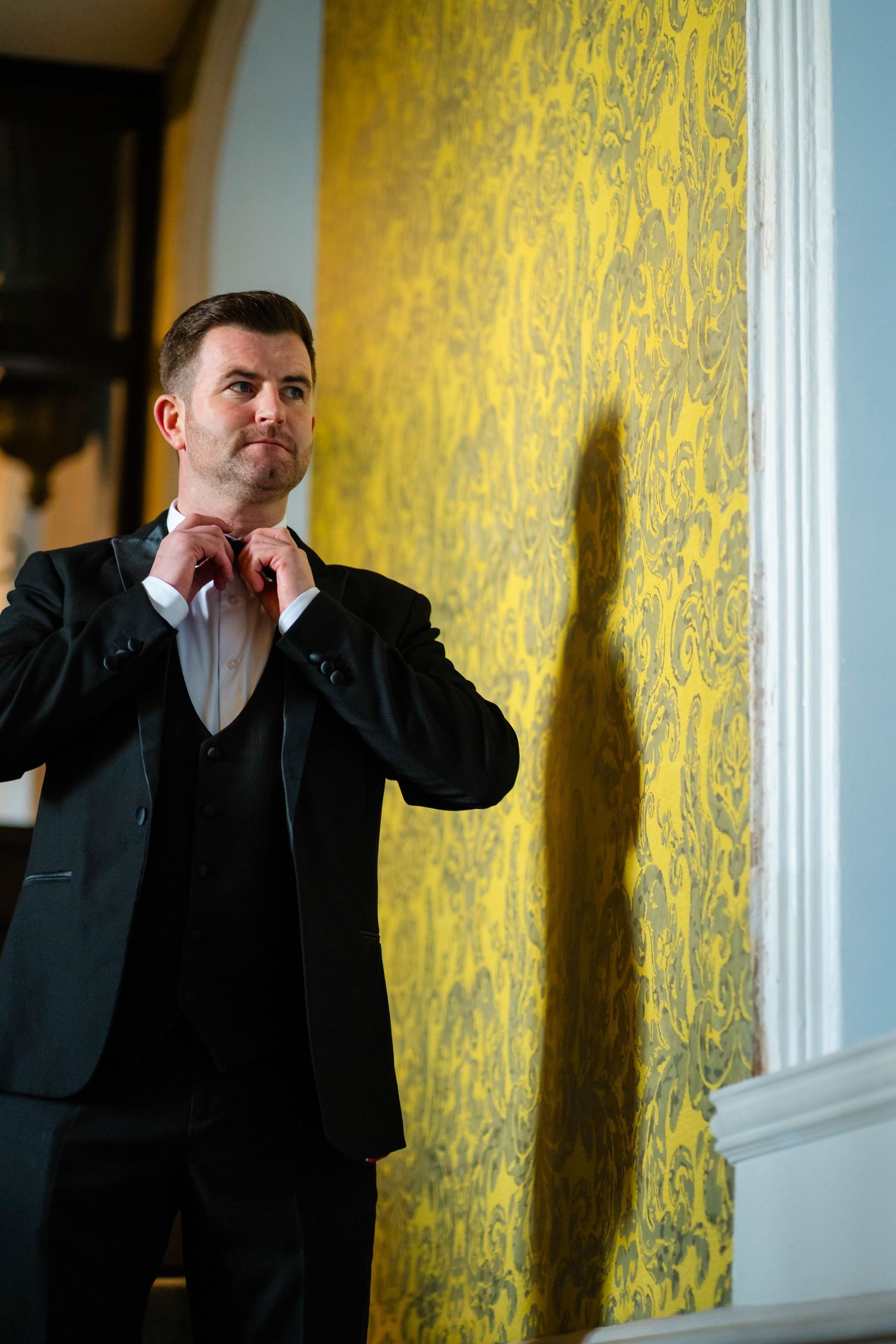 Formal portrait against yellow damask wallpaper in elegant setting.
