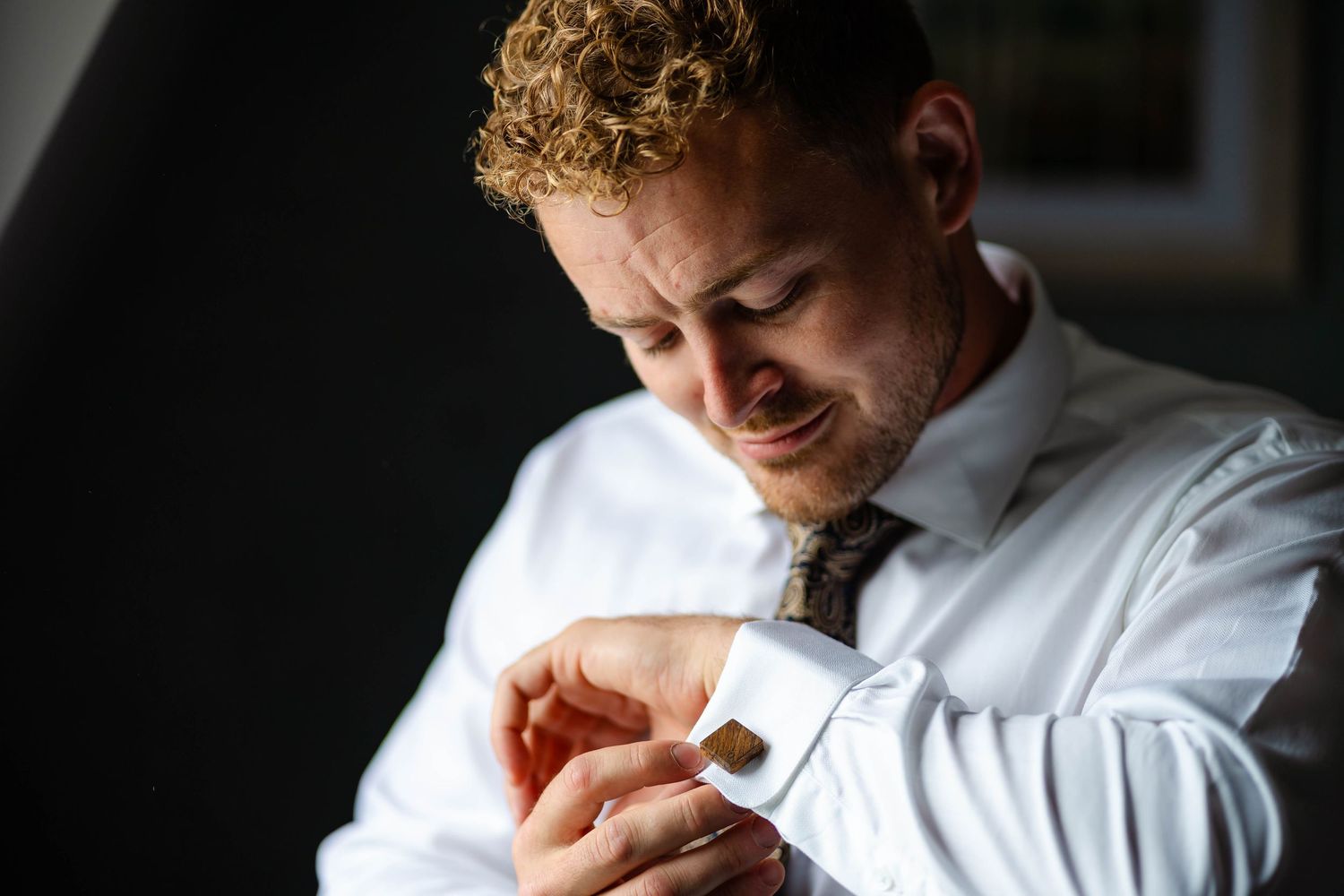Groom in white shirt and tie adjusts his cufflinks while getting ready.