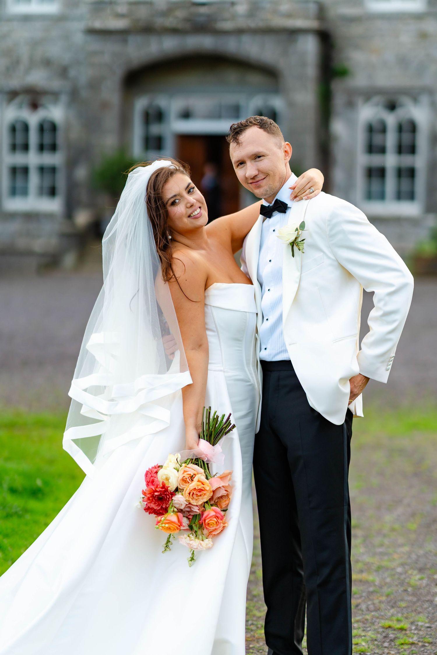 A happy couple poses together outdoors on their wedding day, with the bride in white and groom in formal attire.