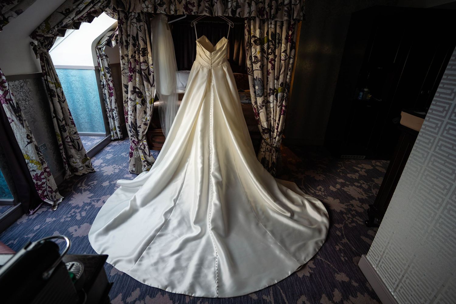 An elegant white wedding dress with a flowing train displayed in a dimly lit room.