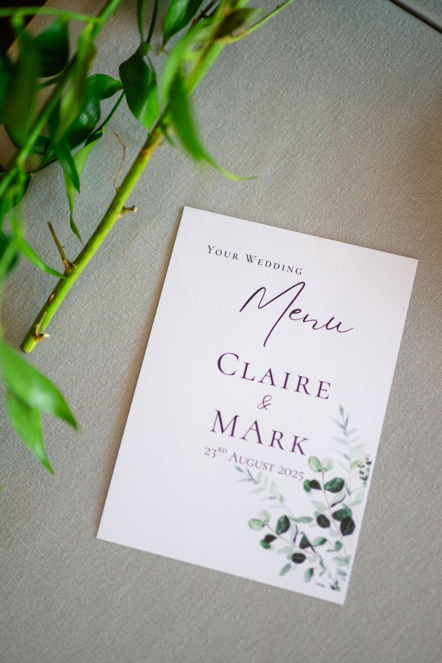 Wedding menu card with floral design and elegant typography photographed with green foliage.