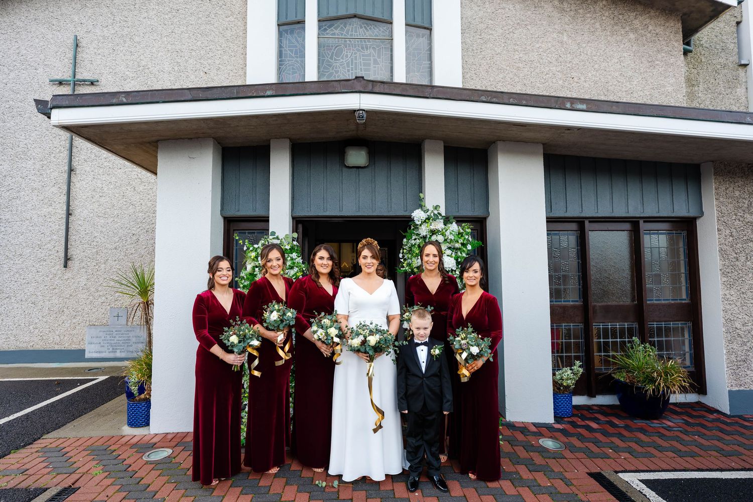 Wedding party group photo outside a modern building with burgundy bridesmaids dresses.