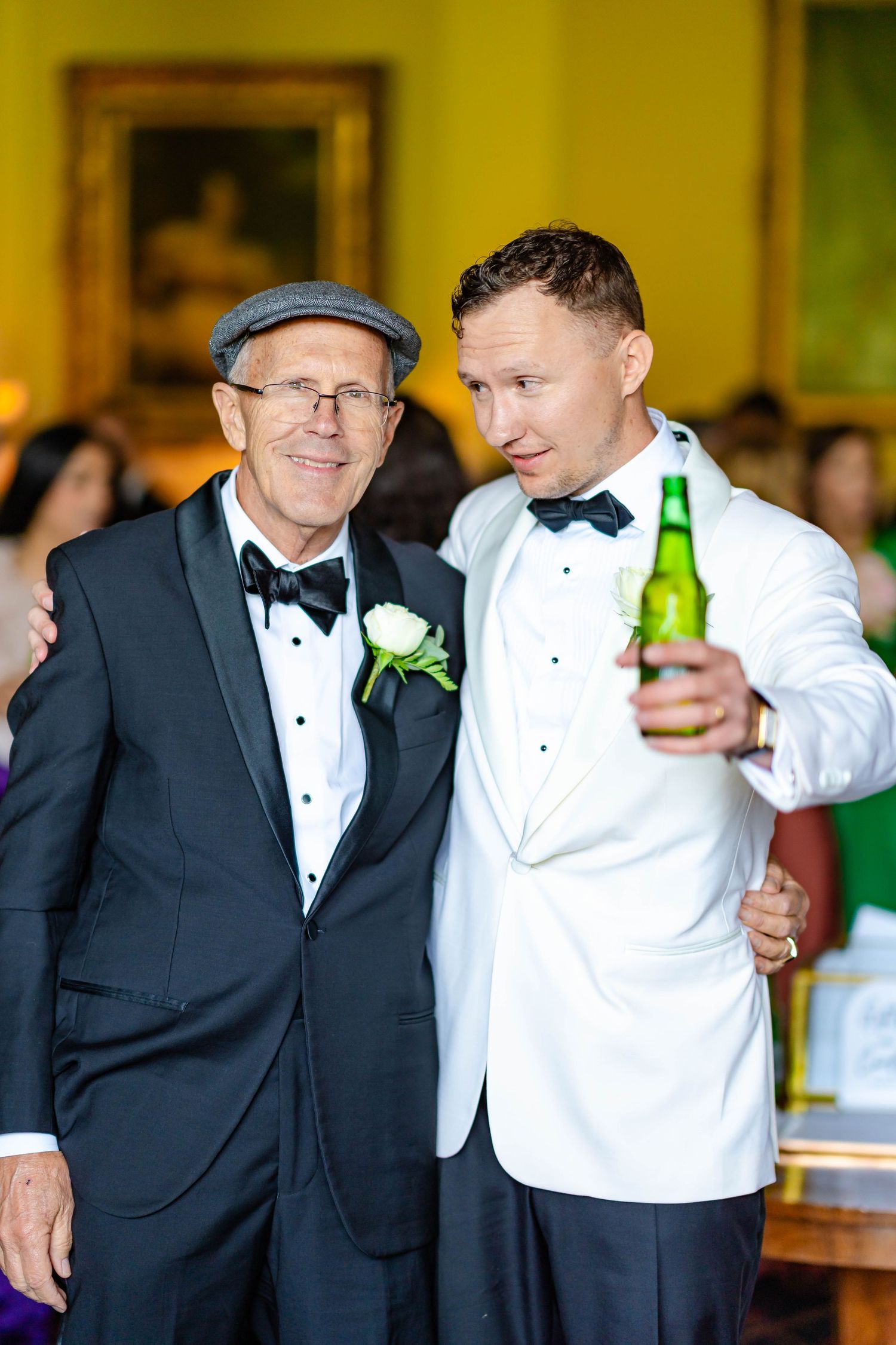 Wedding party members in tuxedos and white jackets share laughs during formal reception celebration.