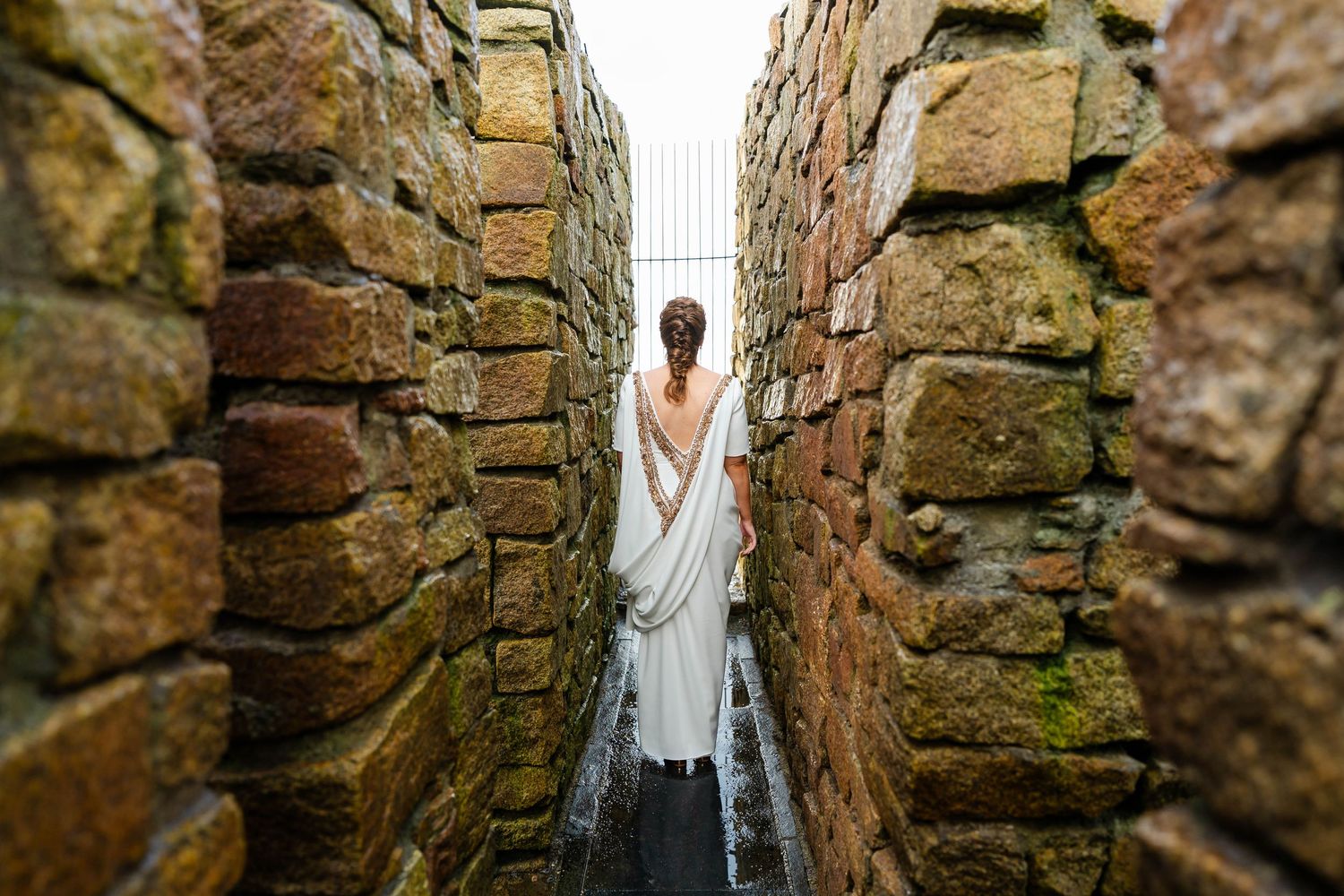 White wedding dress flowing between ancient stone walls in a narrow passageway.