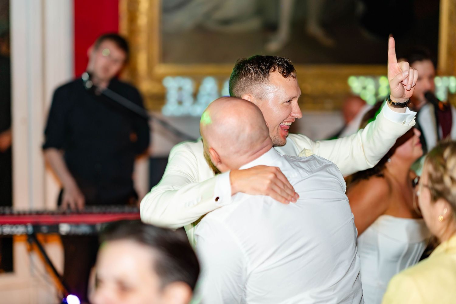 People in white clothing dance and celebrate energetically on a dance floor at an indoor event.