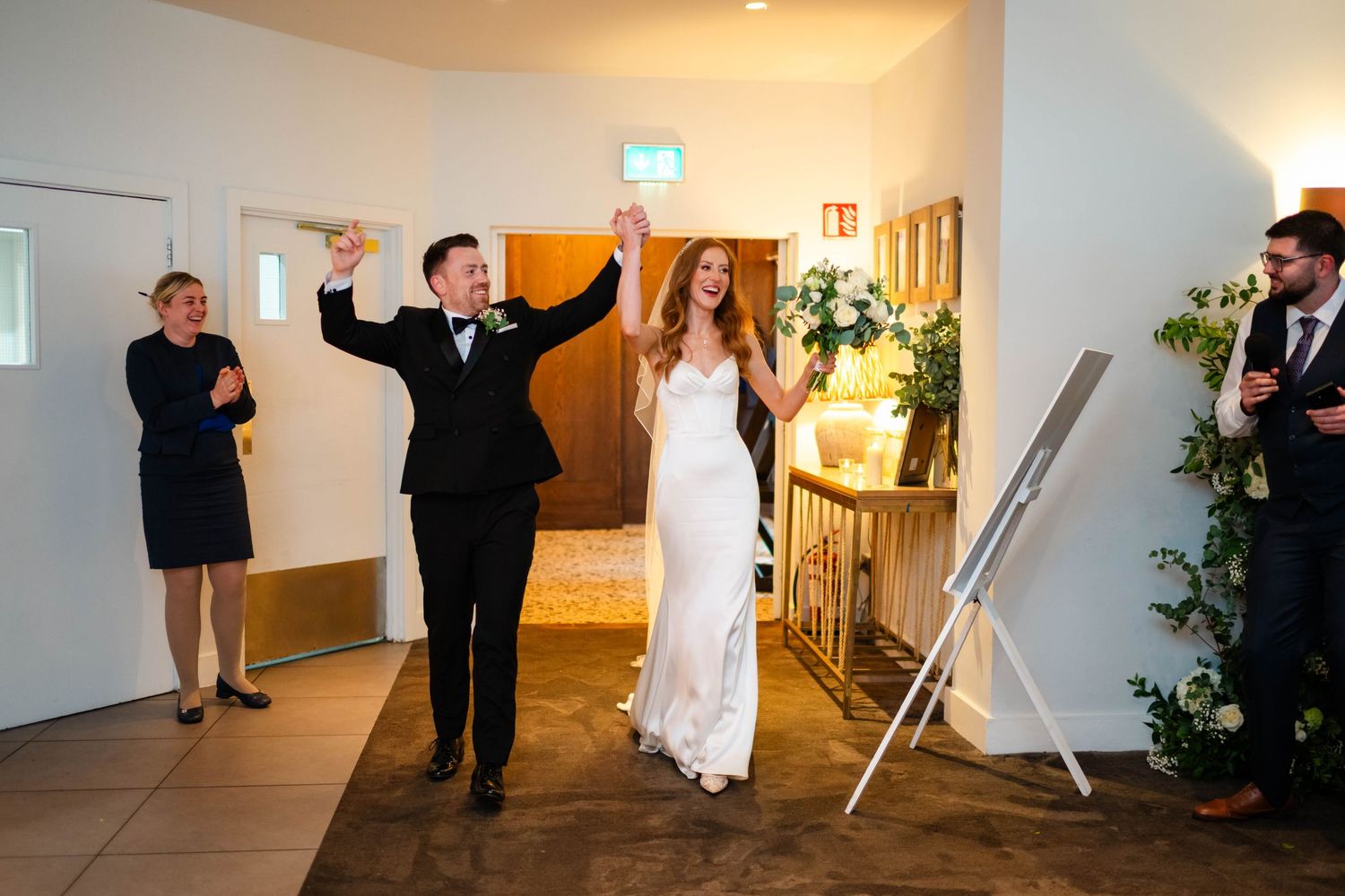 Wedding guests dancing and celebrating at a reception in a bright indoor venue.