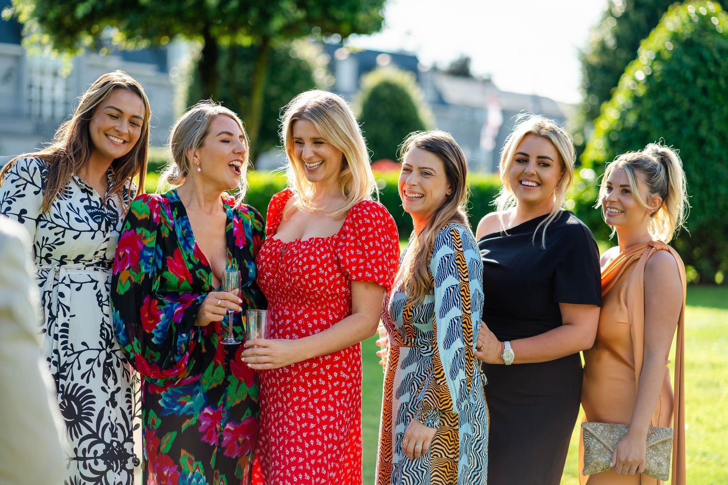 Wedding guests in colorful dresses laugh and celebrate outdoors.