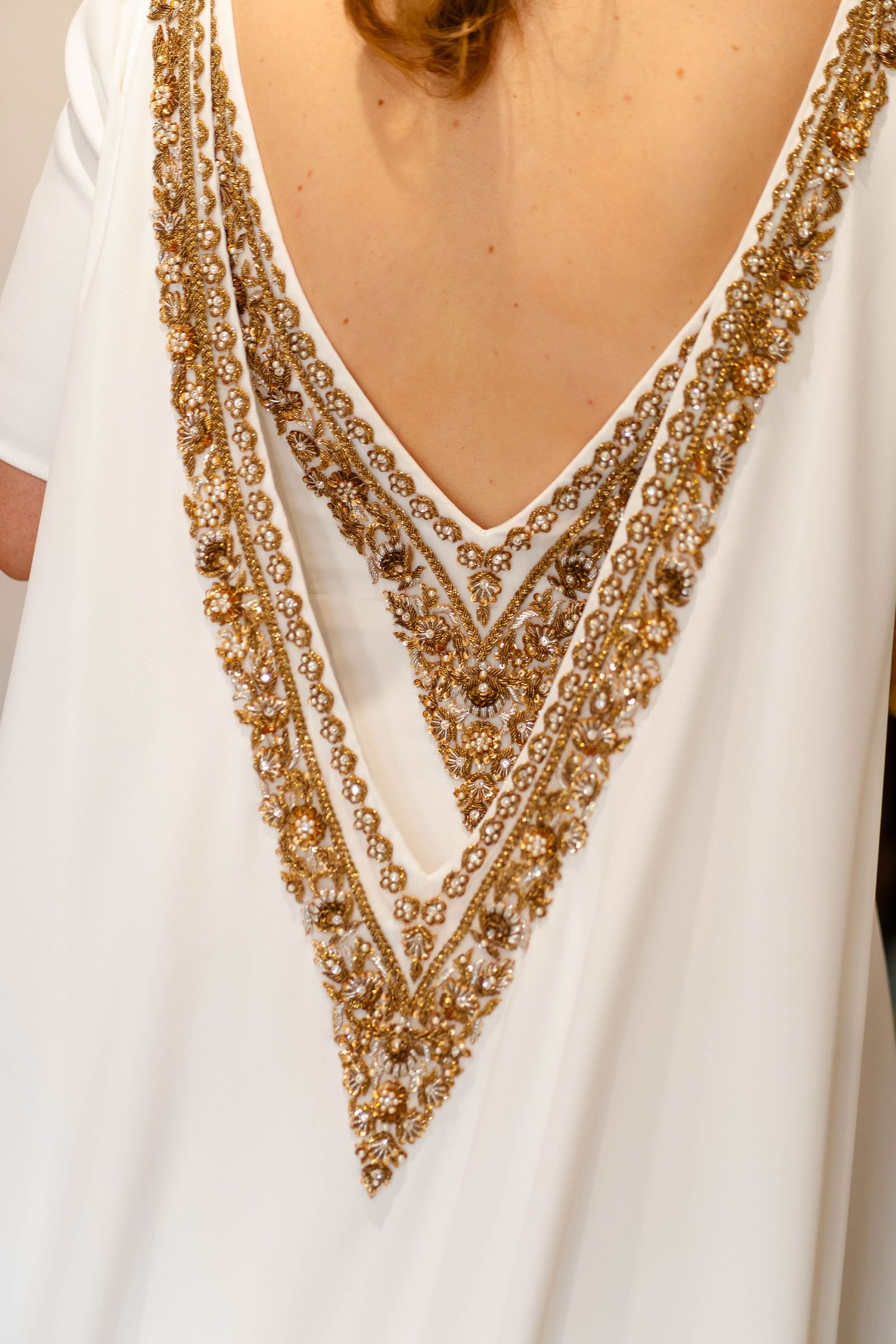 Detailed view of gold beaded v-neck embellishment on white wedding dress.