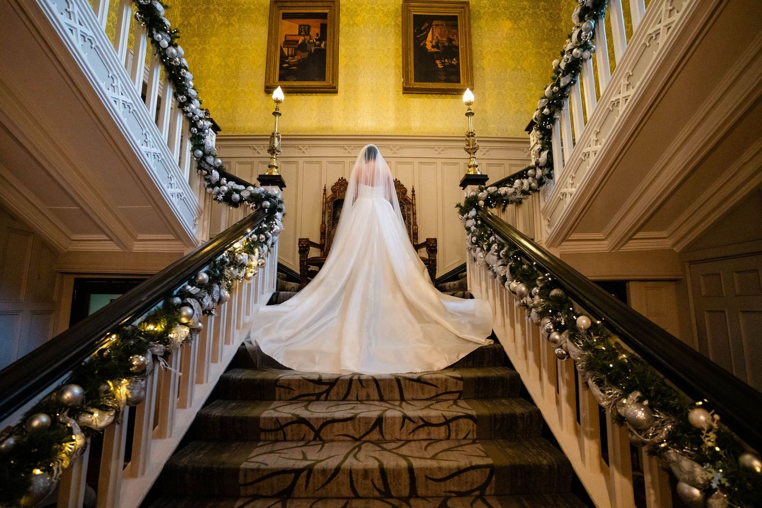 A stunning wedding dress with a long train photographed on an elegant staircase decorated with holiday garland.