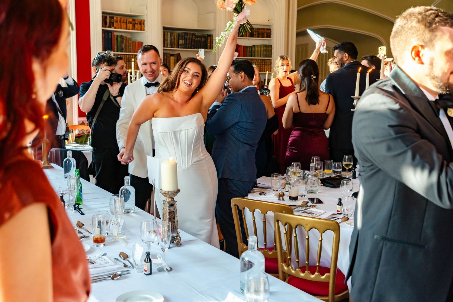 Wedding guests mingle and socialize during an elegant indoor reception with white tablecloths and decorative settings.
