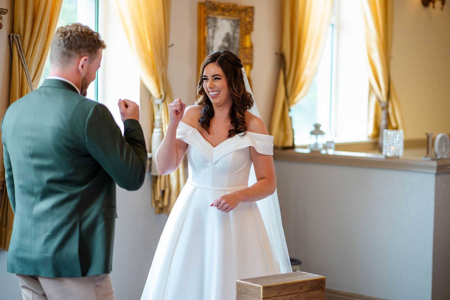 Wedding couple shares a joyful moment in an elegant room with golden curtains and ornate decor.