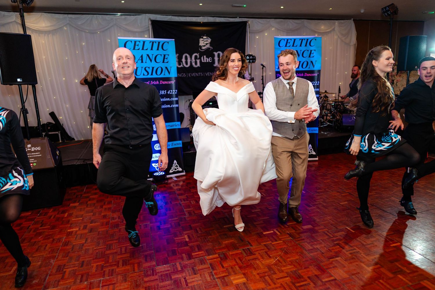 Wedding party dances enthusiastically on red dance floor during reception celebration.