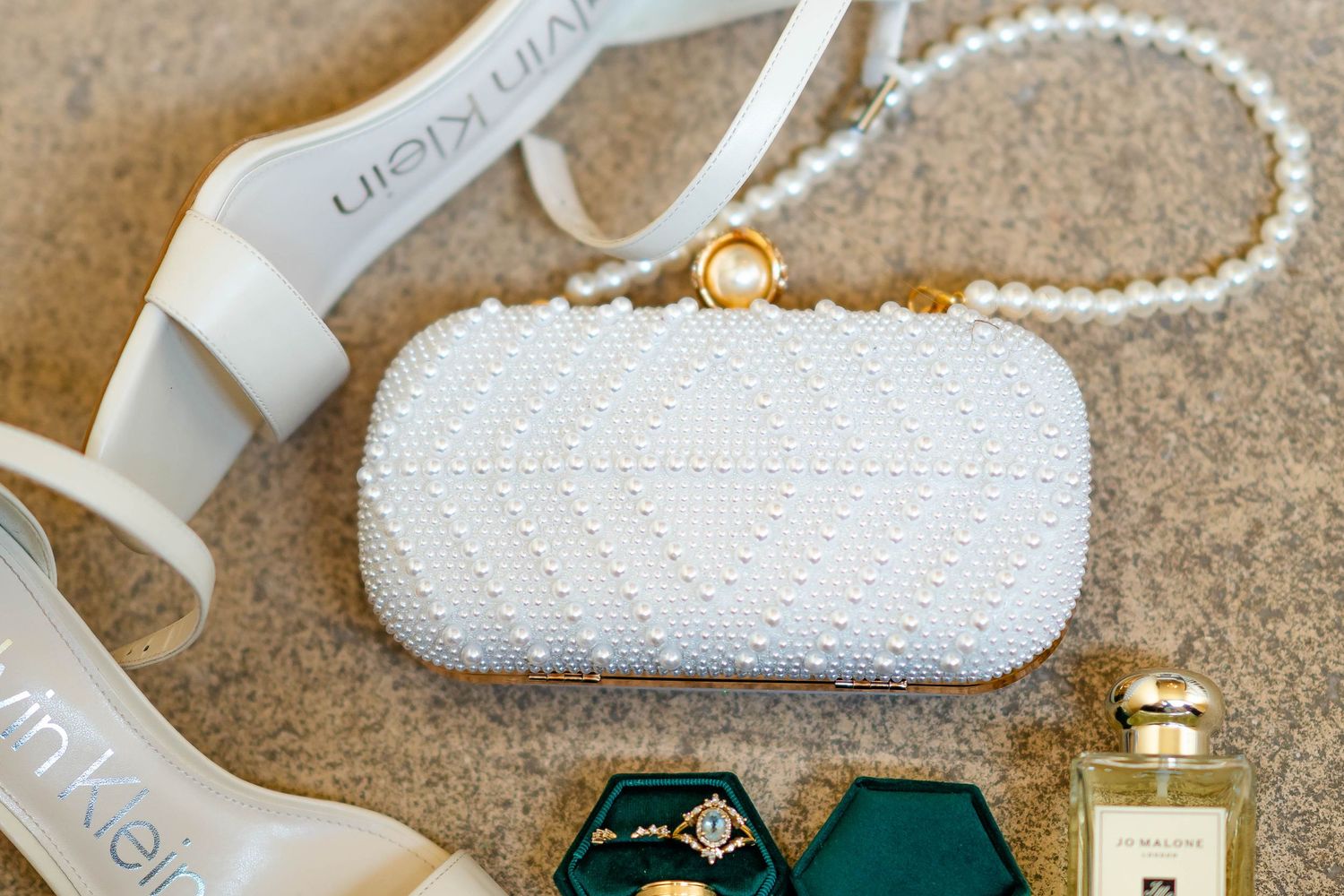 White beaded clutch purse with pearl strap displayed alongside green jewelry box and perfume bottle on beige surface.