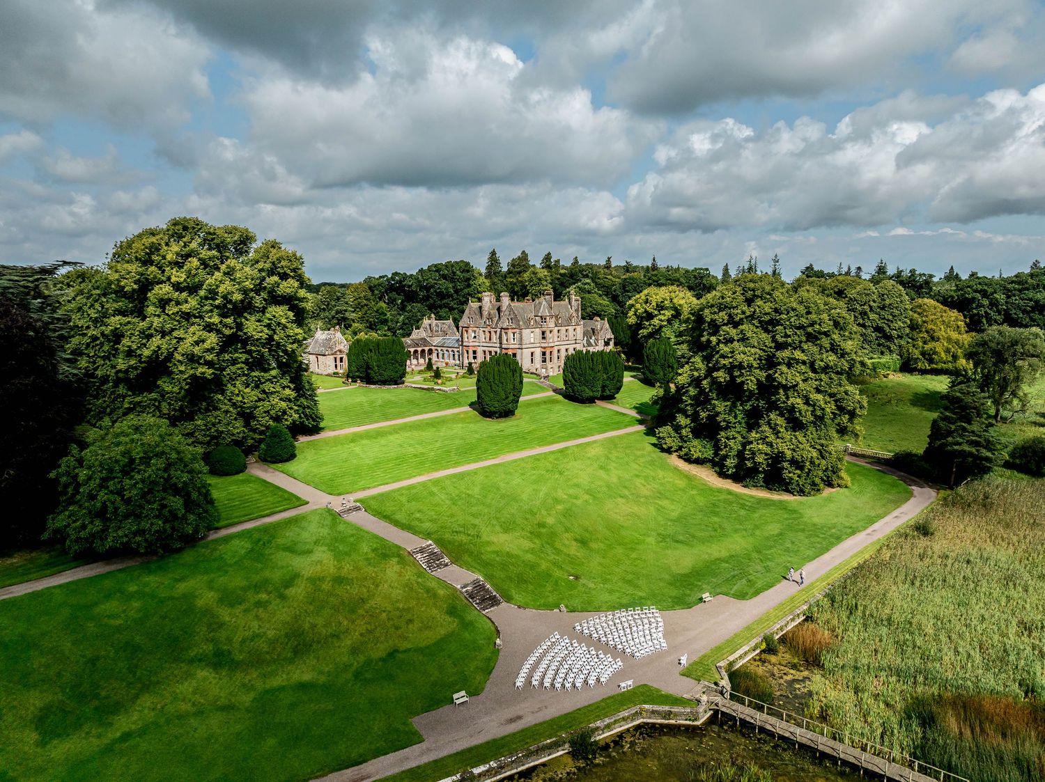 Aerial view of a grand stone manor house surrounded by rolling green countryside.