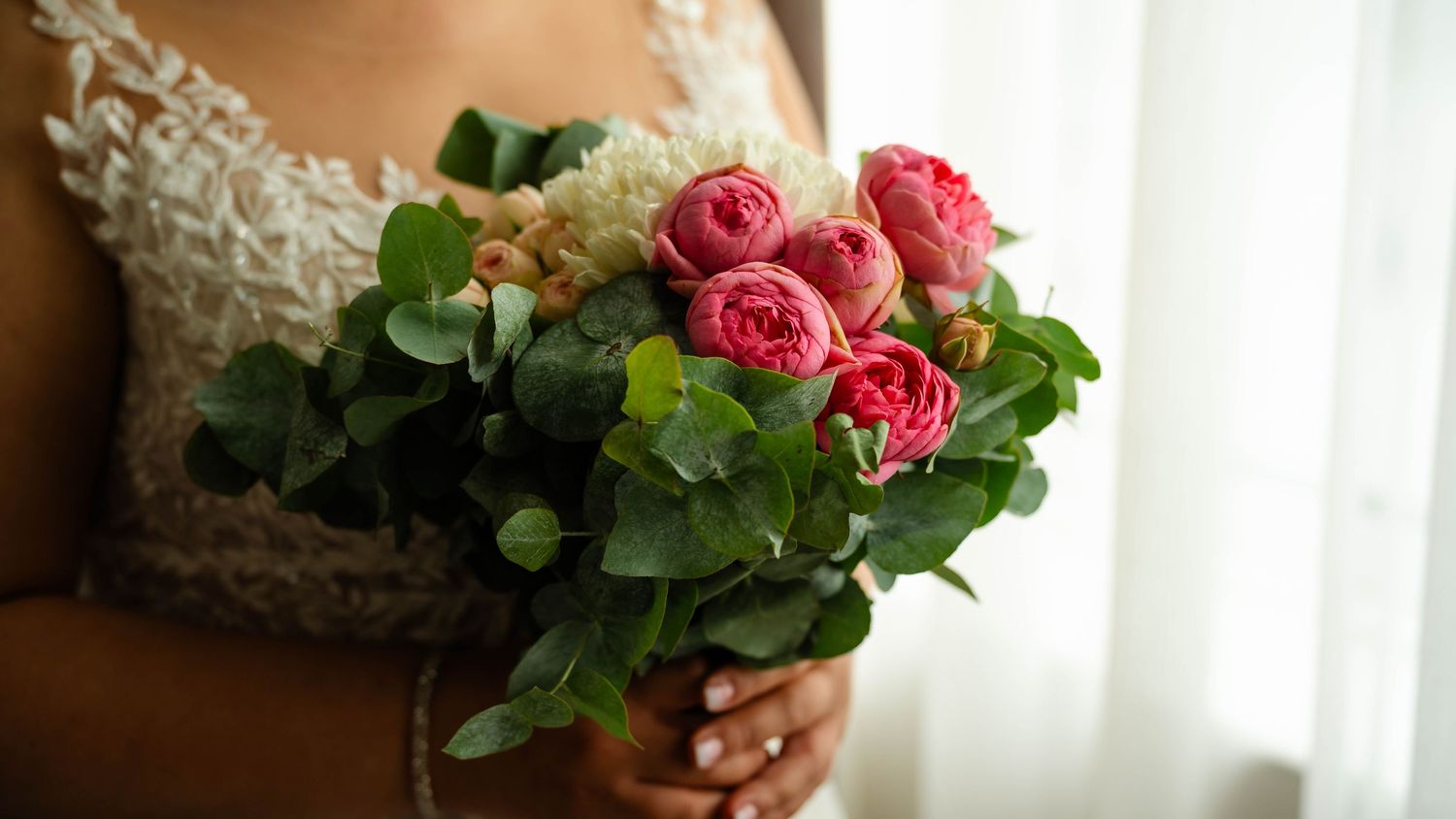 Wedding bouquet with pink roses and greenery against a light background.