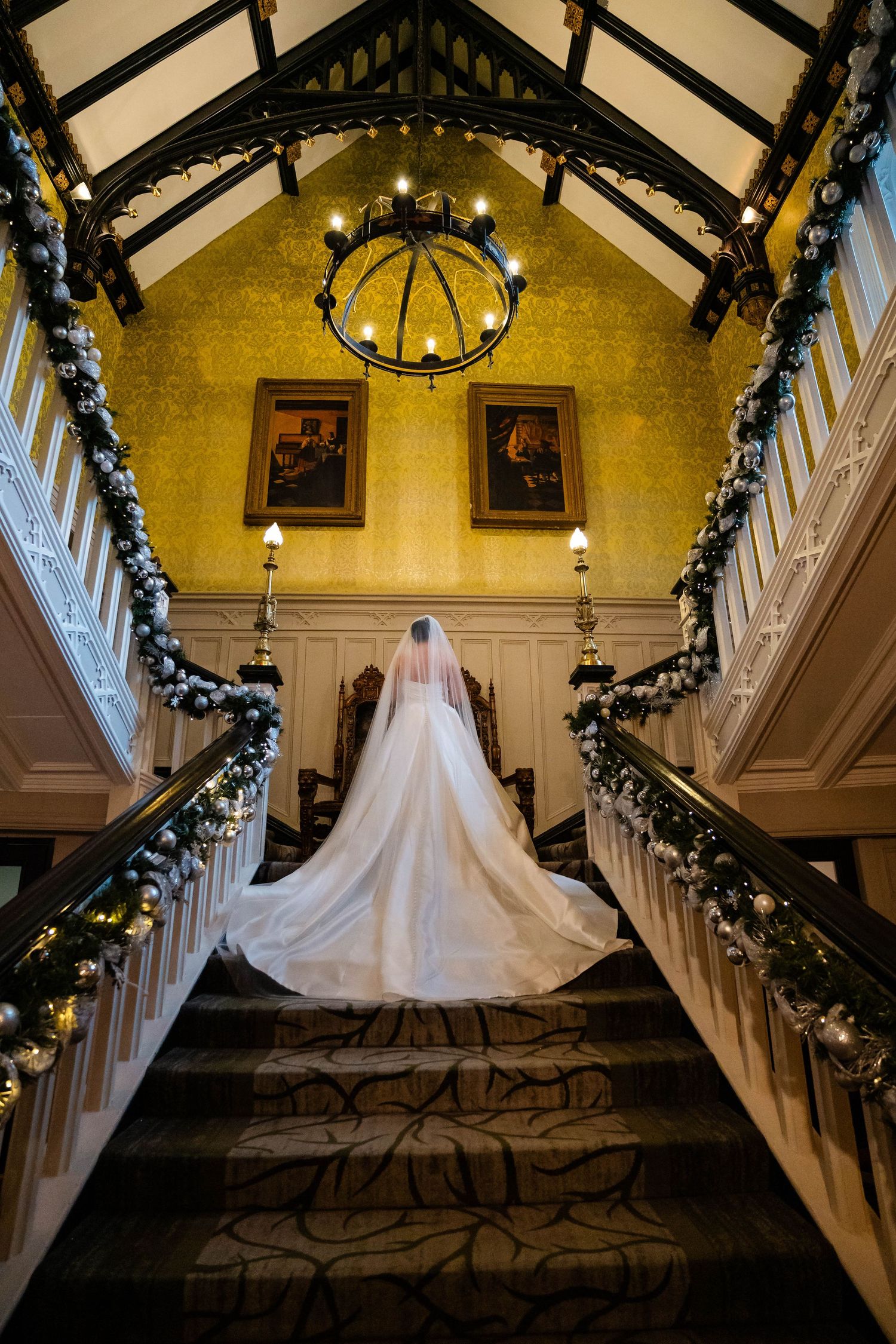 Elegant wedding dress with flowing train photographed on grand staircase with festive garland decor.
