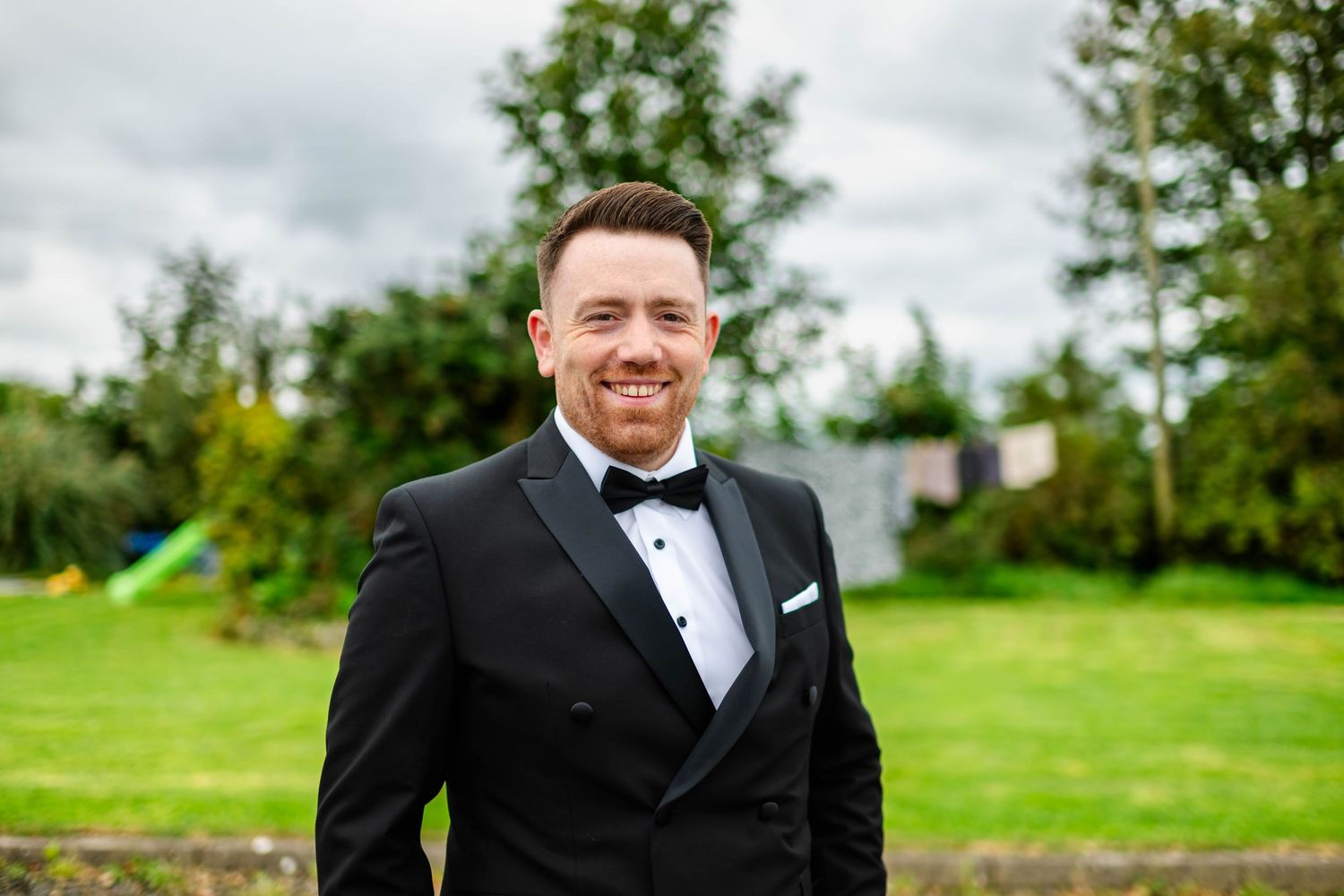 Groomsmen smiling and posing outdoors on a green lawn in formal attire.