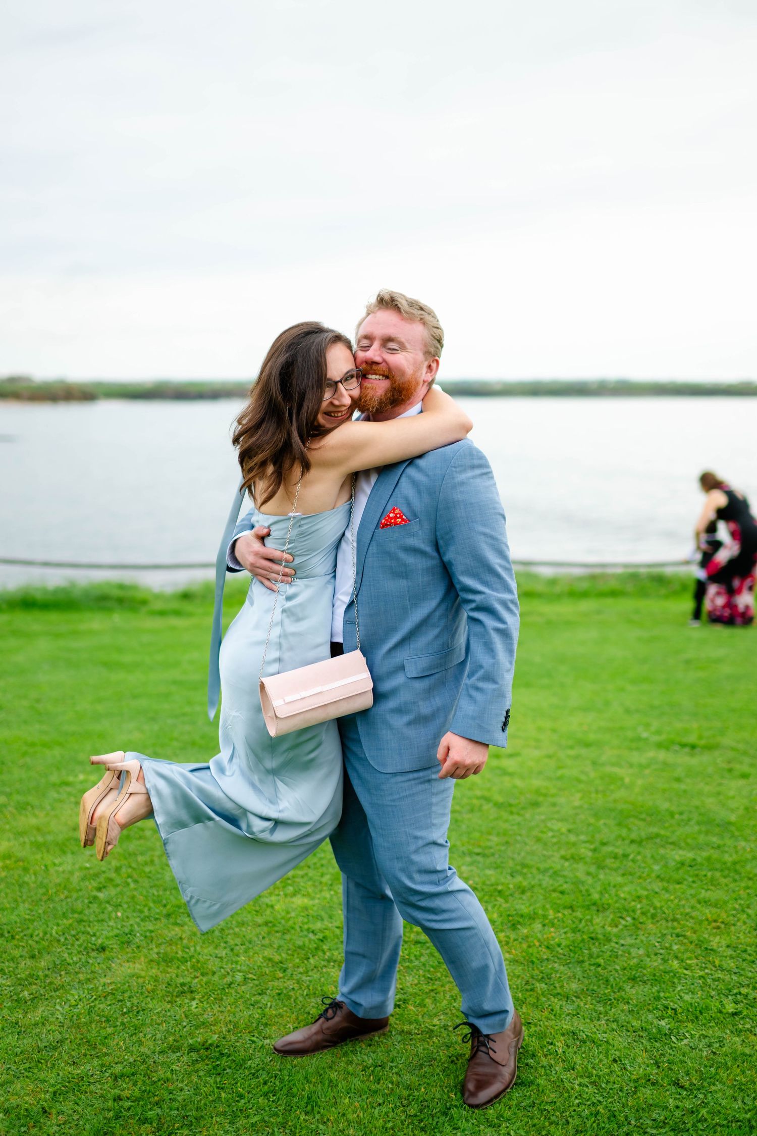 Couple in formal wear share romantic dance on green lawn by the water.