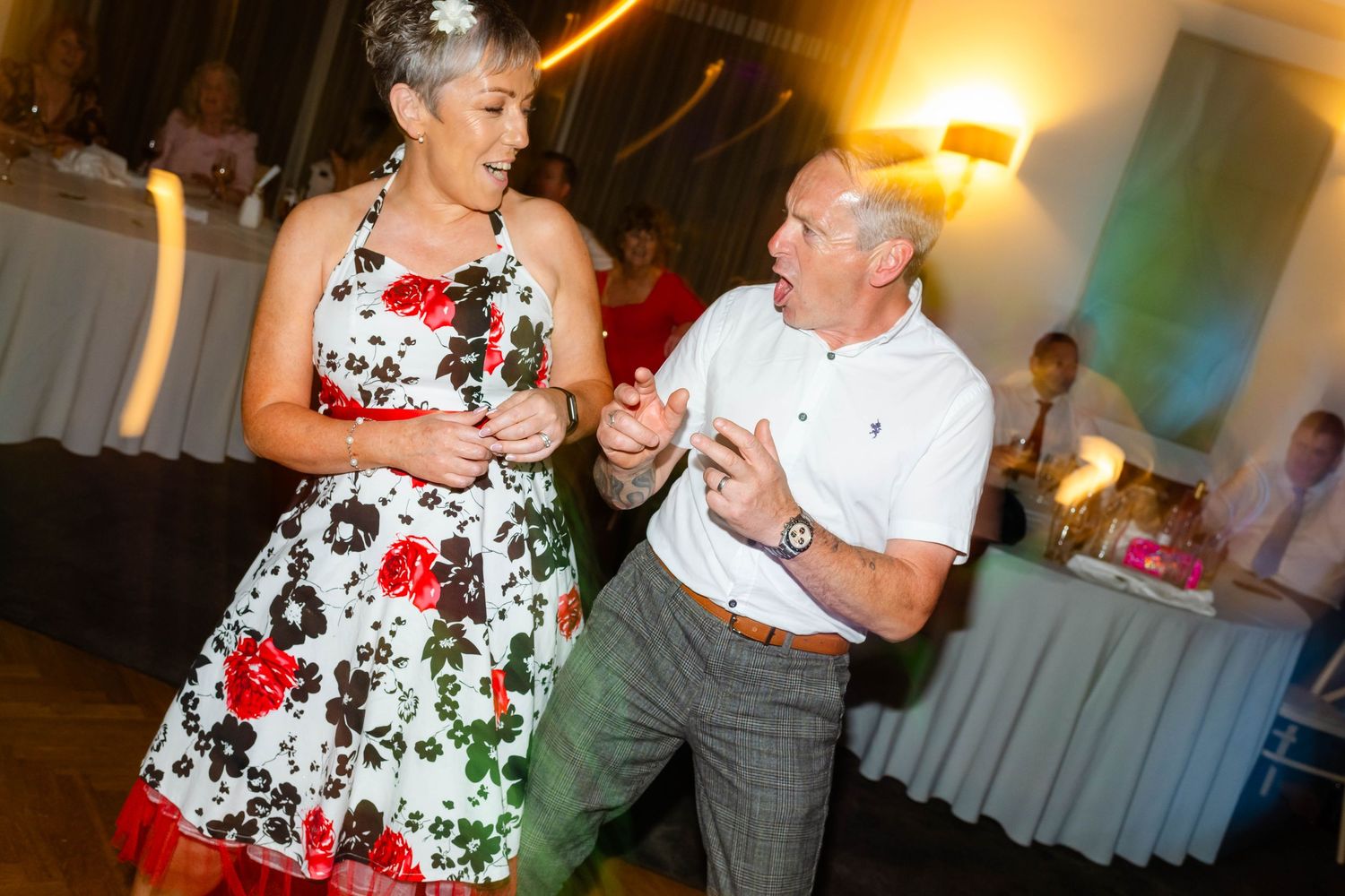 People dancing and celebrating at a lively wedding reception with warm lighting and floral decor.