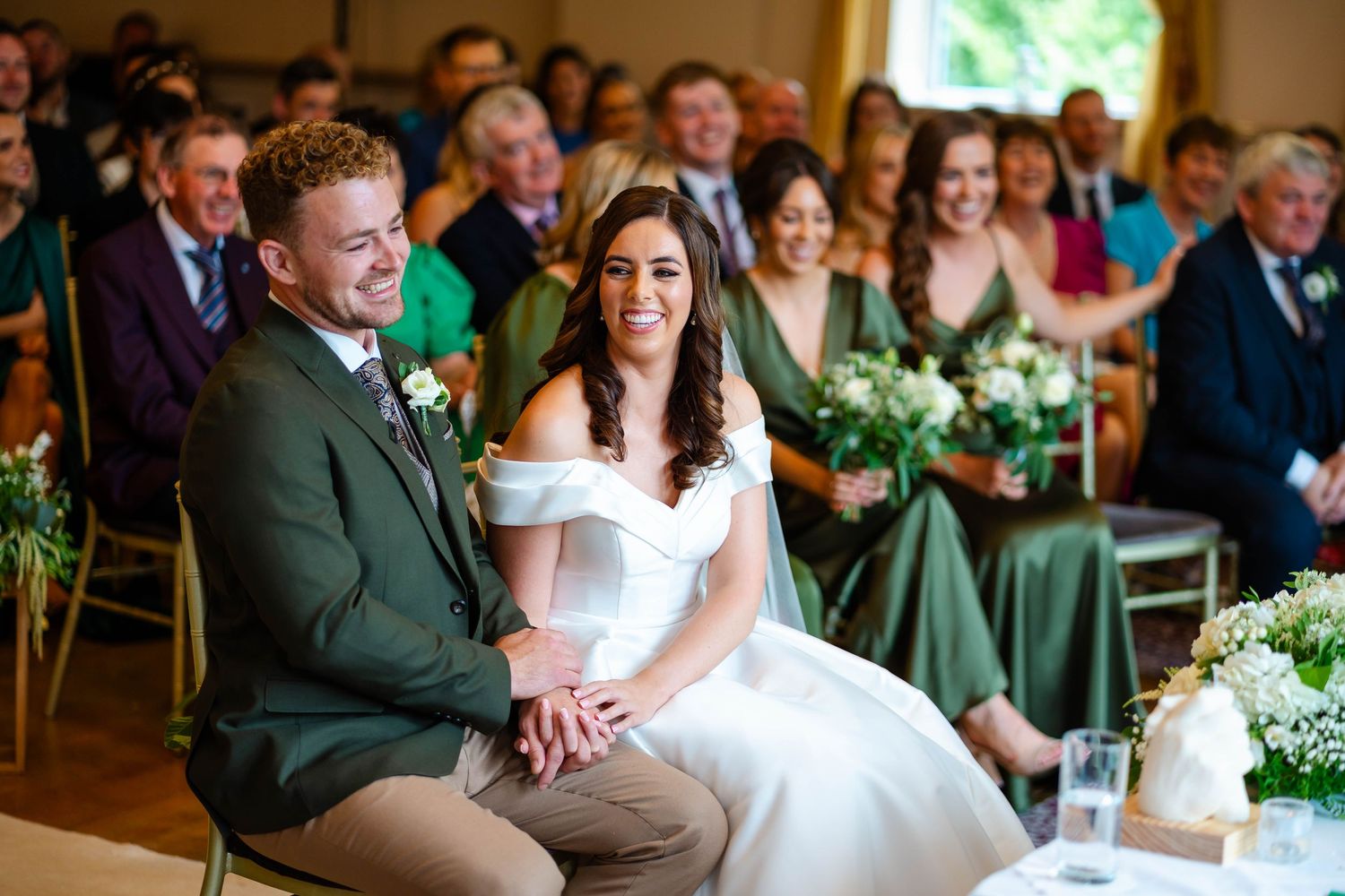 Wedding ceremony in progress with guests seated in rows and green accents throughout the venue.
