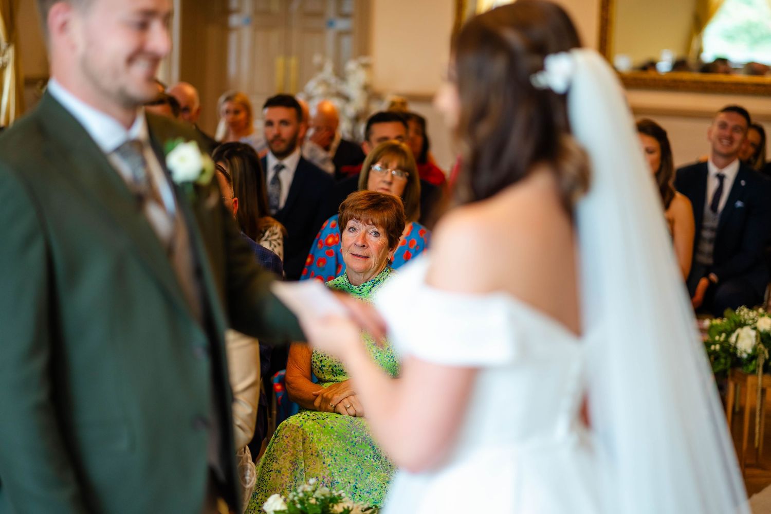 Wedding ceremony in progress with guests seated and green floral decorations.