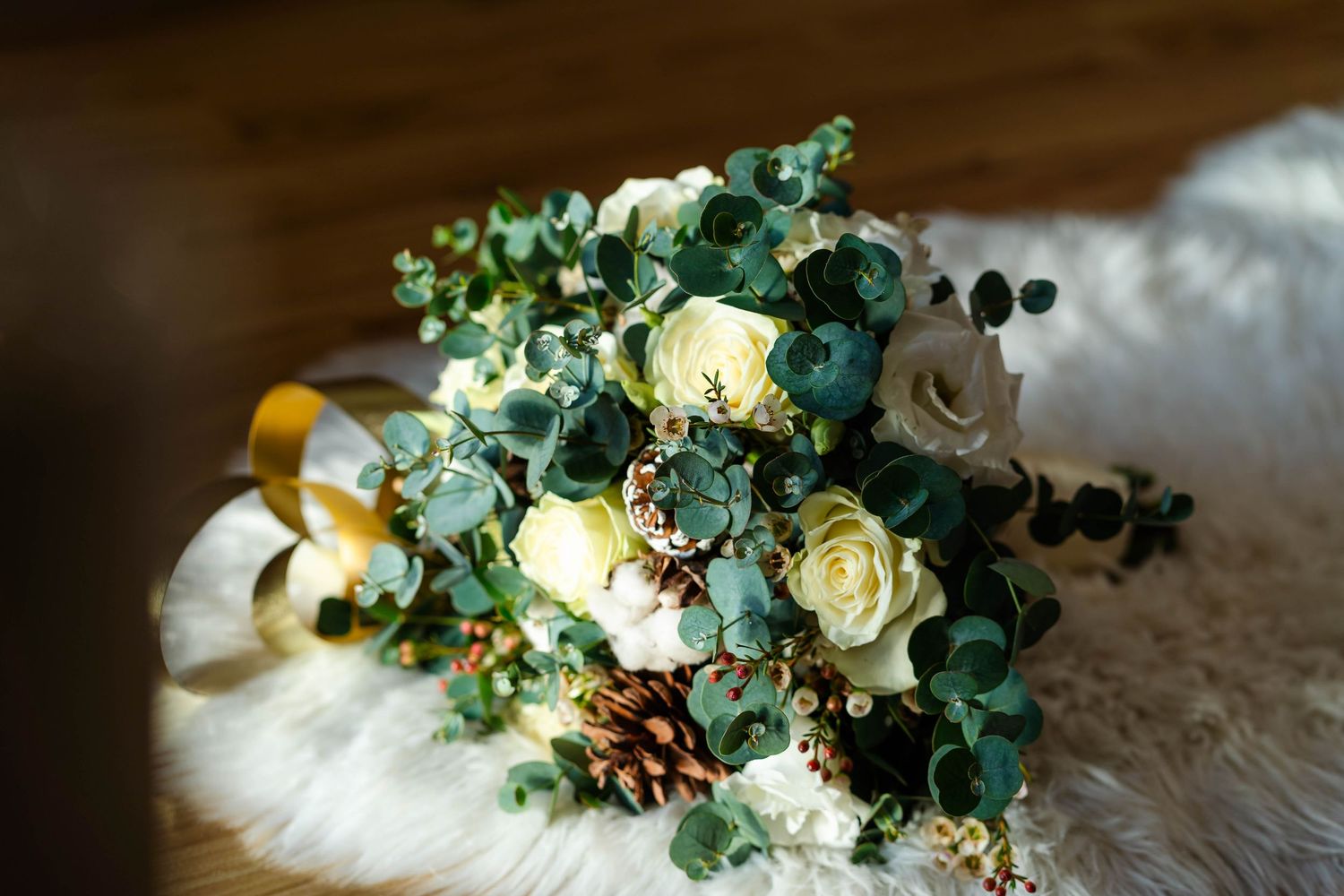 Wedding bouquet with white roses and eucalyptus leaves on white fur background.