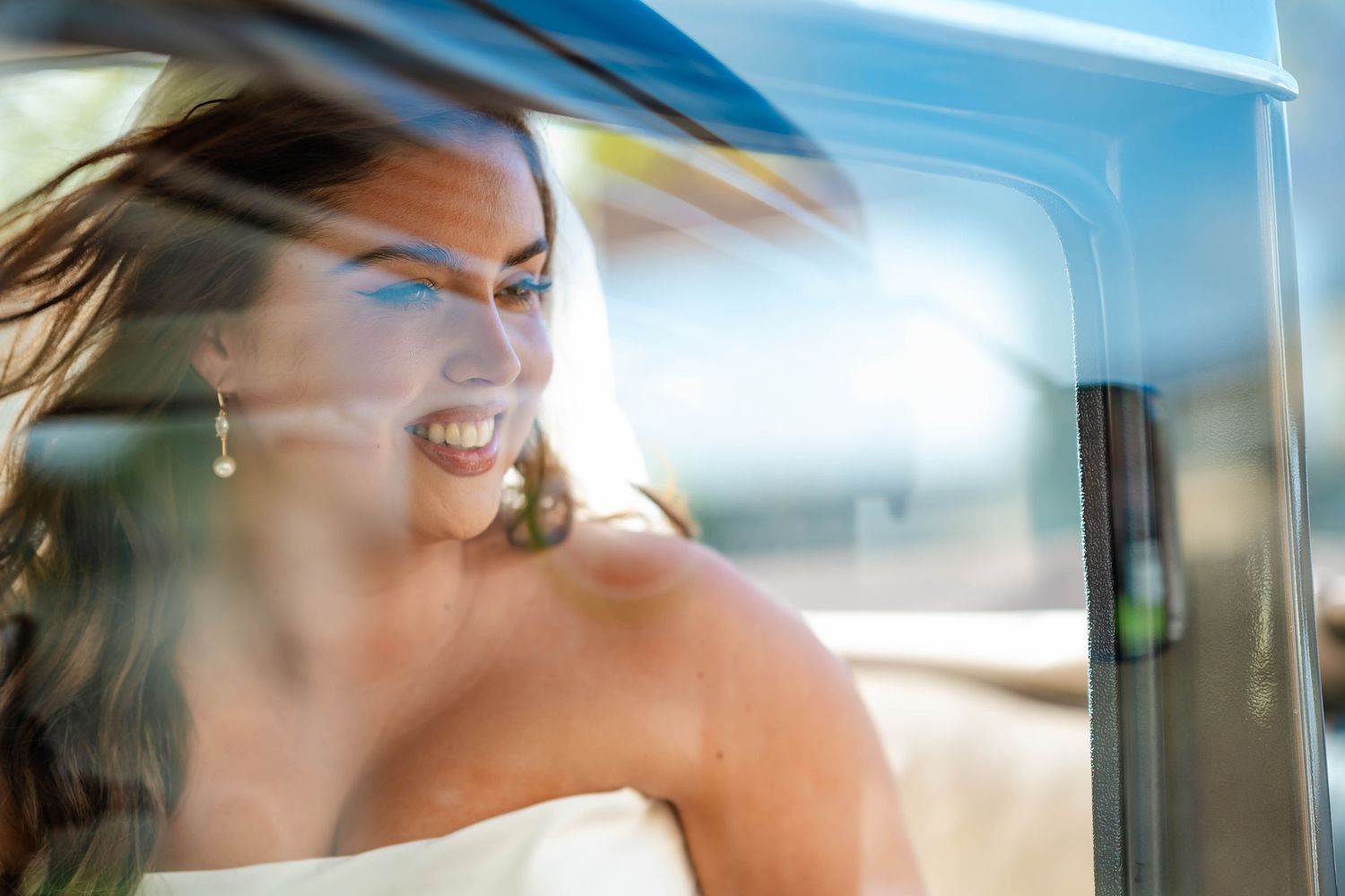 A person smiles while sitting in a car with sunlight streaming through the window creating a bright, ethereal effect.