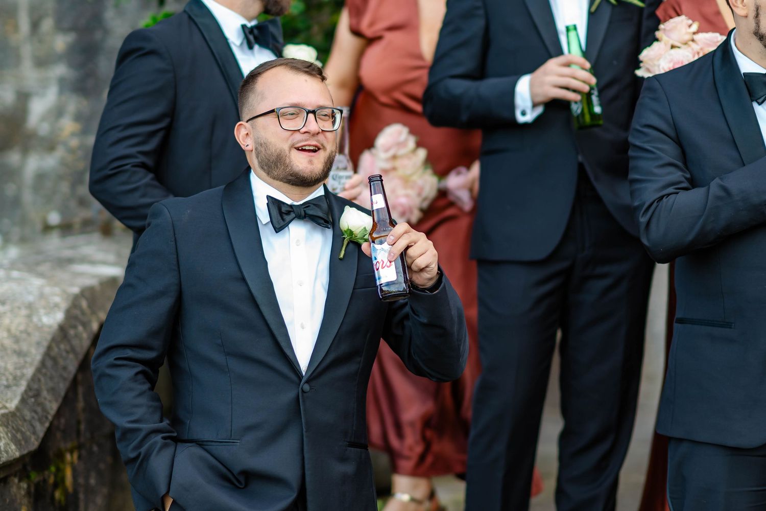 Wedding guests in formal attire gather outdoors for a celebration with drinks and conversation.