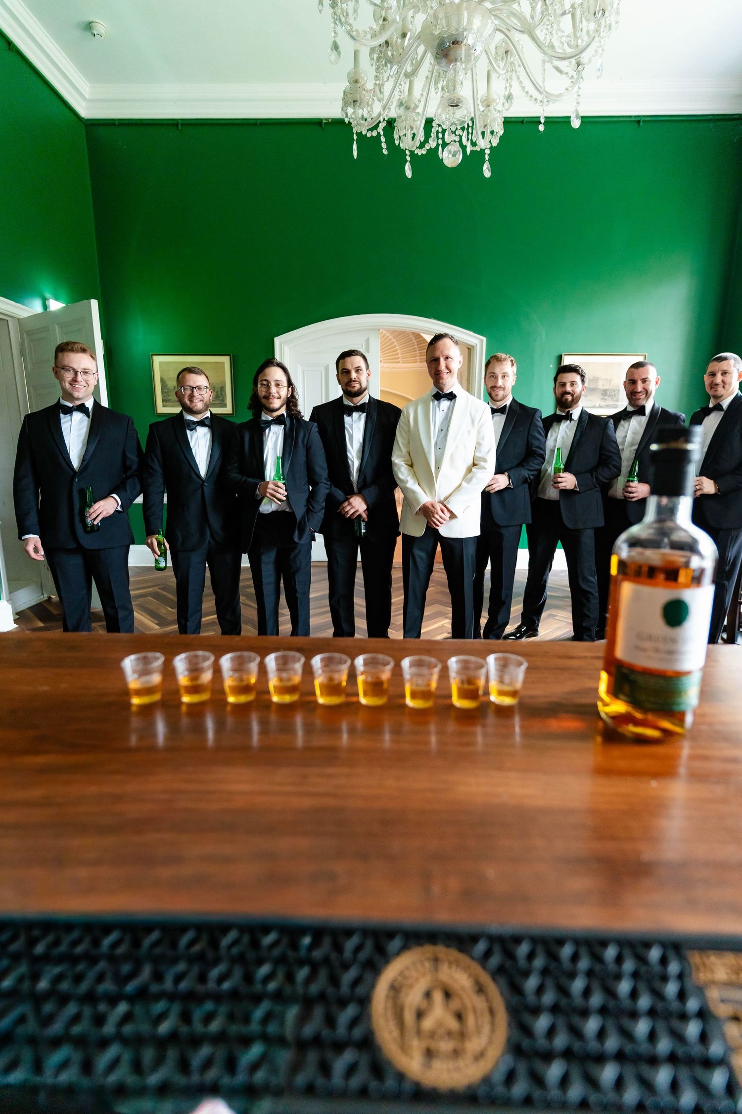 A sequence of photos showing groomsmen in black suits lined up next to a wooden table with whiskey glasses.