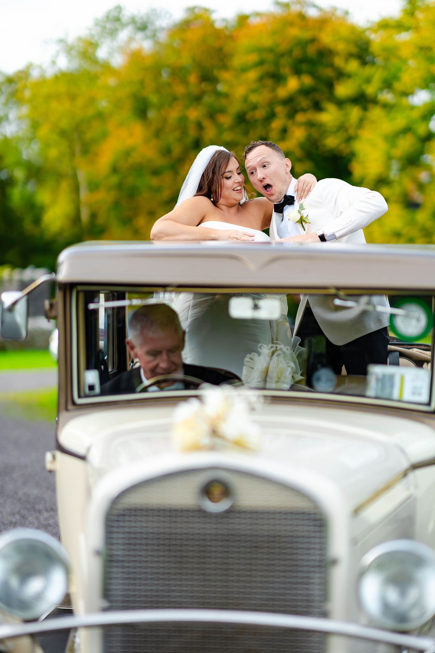 A couple shares a romantic moment in a vintage cream-colored classic car during an autumn wedding photoshoot.