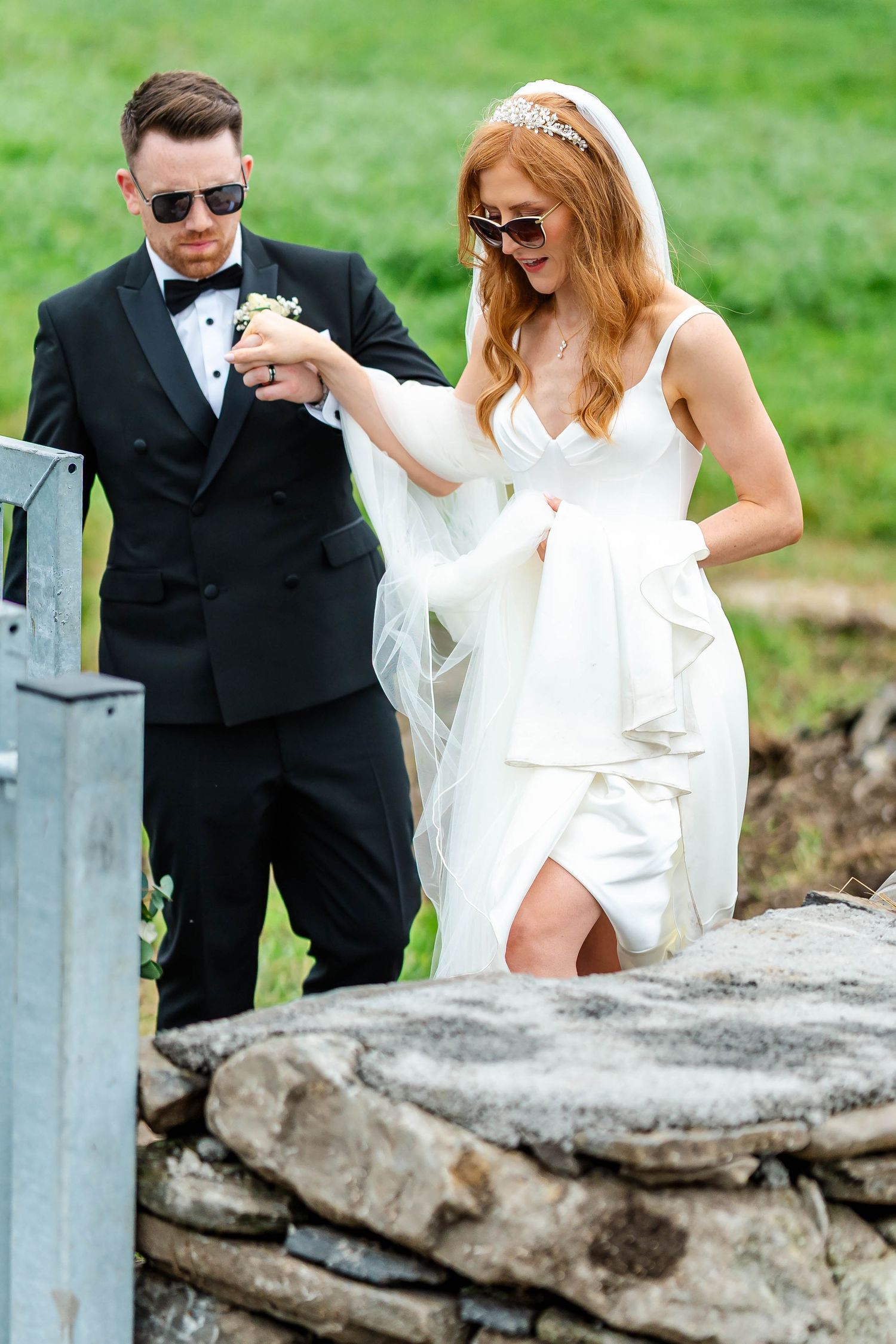 Wedding couple carefully navigates stone wall path in formal attire.