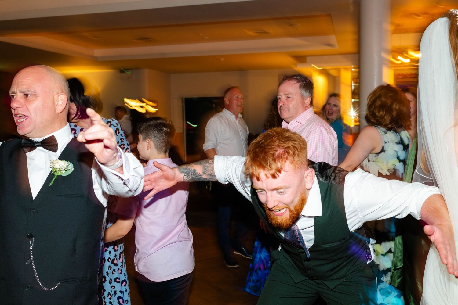 Wedding guests performing synchronized dance moves at indoor reception.