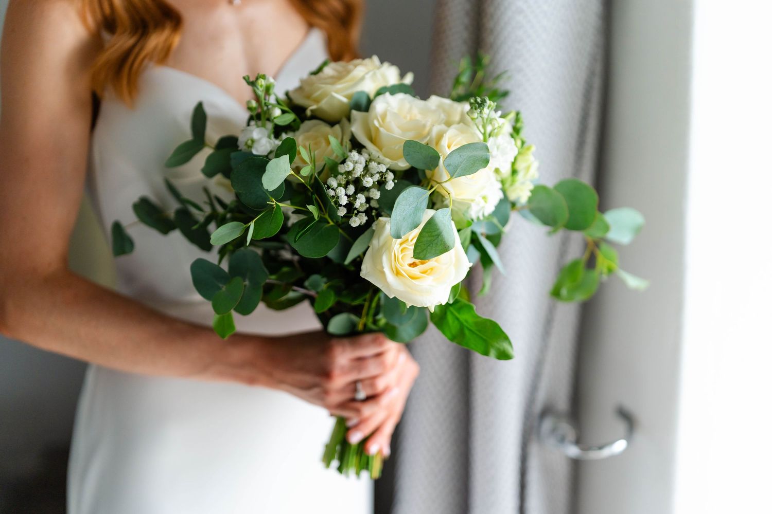 A bridal bouquet of white flowers and green foliage against a light background.
