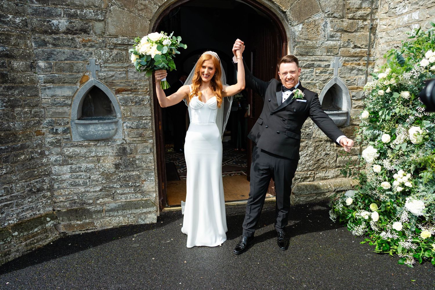 Stone church exterior with gothic archways and white floral decorations.