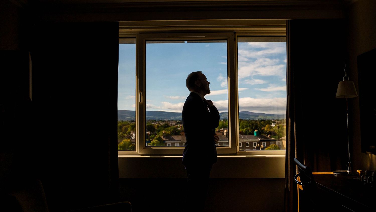 Panoramic window view of landscape with dramatic clouds and silhouetted figure.