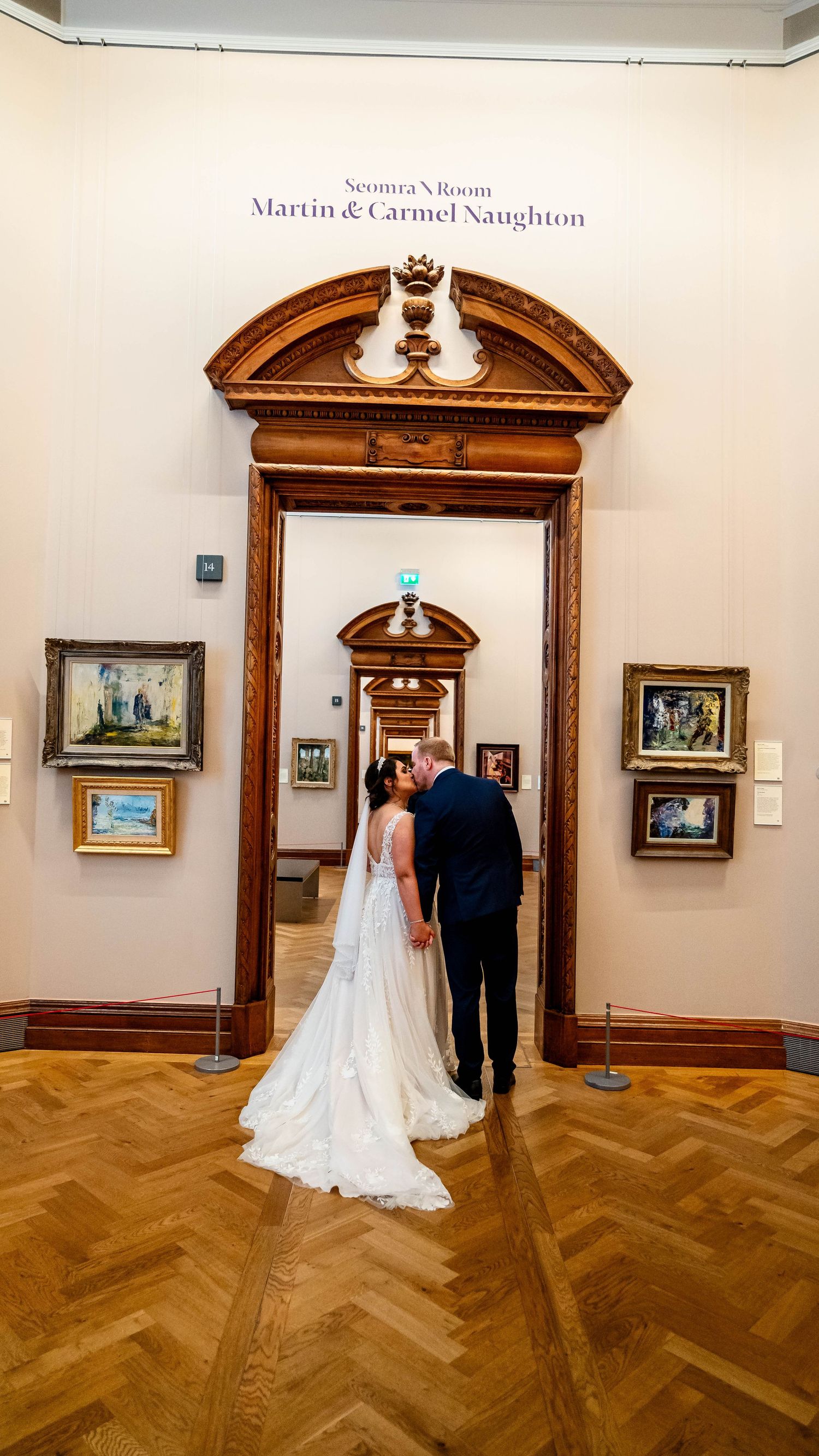 Art gallery interior with ornate wooden archways and framed paintings on white walls.