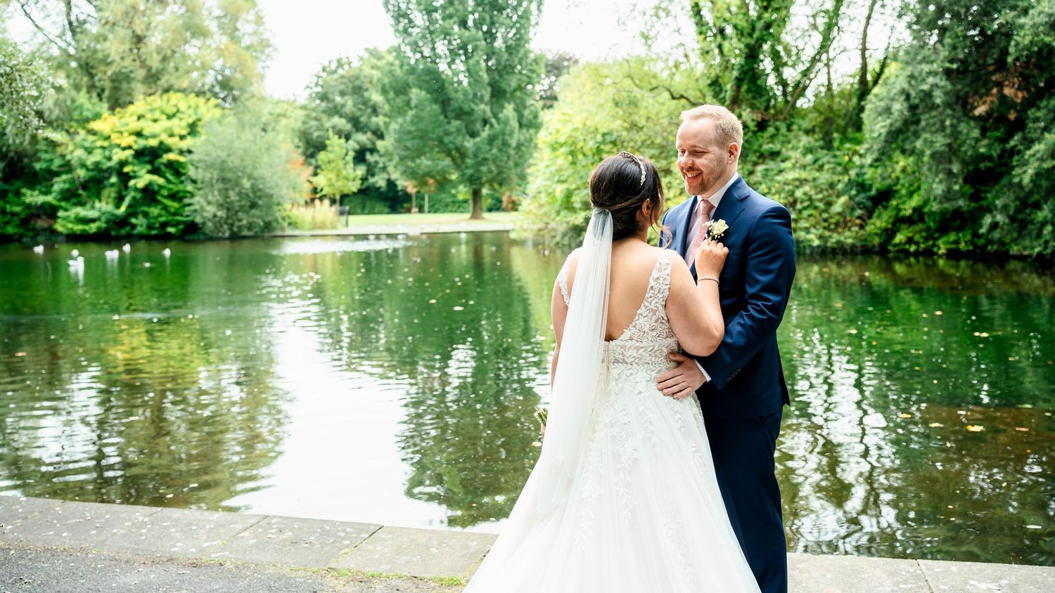 Panoramic wedding scene by a serene lake surrounded by lush summer greenery.