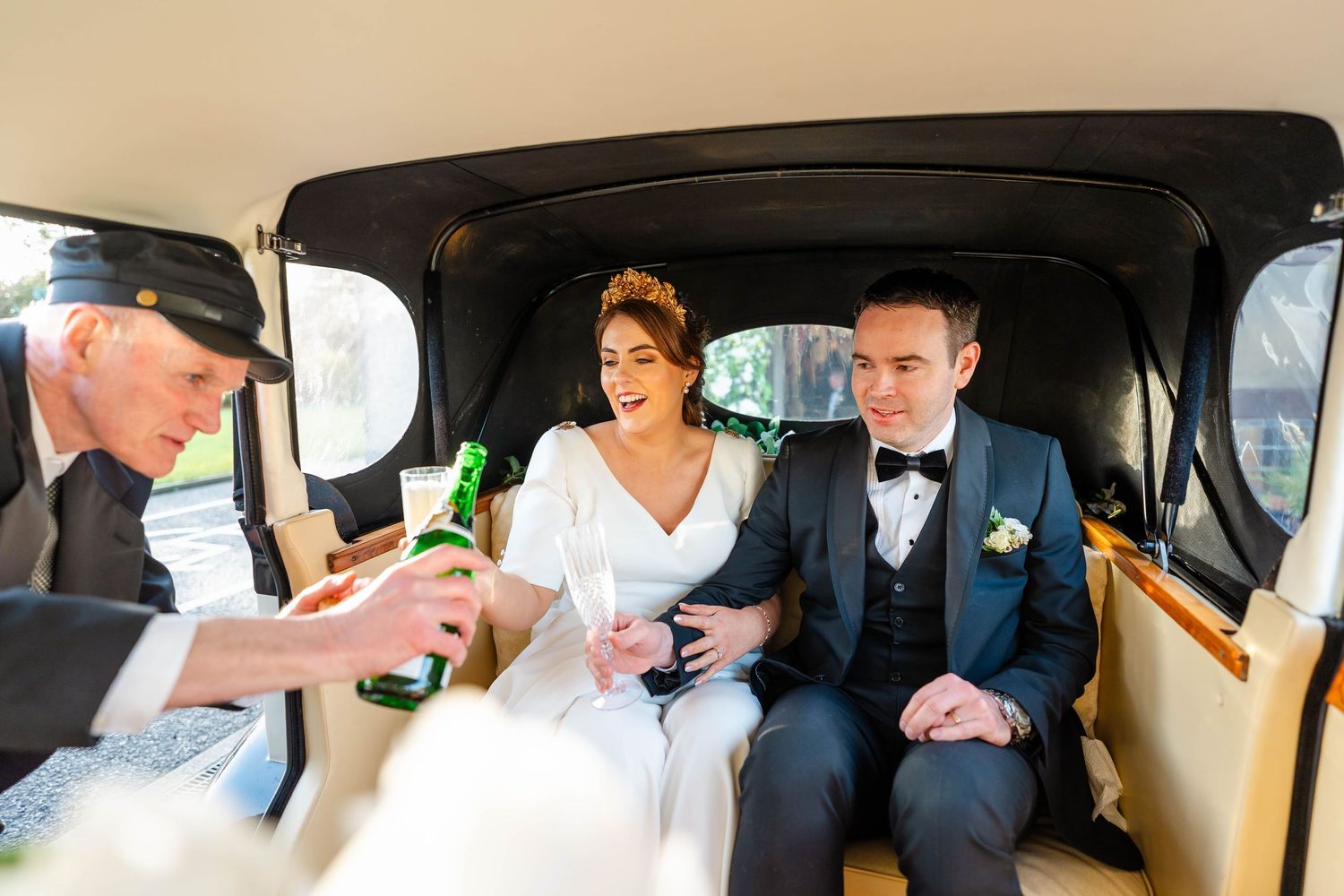 Wedding party celebrating with drinks inside vintage car interior.