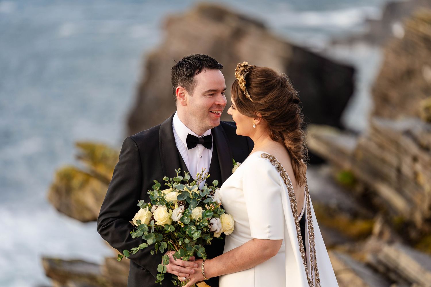 Romantic wedding couple embracing on a rocky coastal landscape with ocean views.