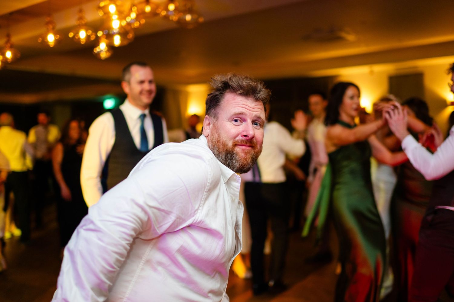 Energetic dancers moving in sync during a wedding celebration with dramatic lighting.