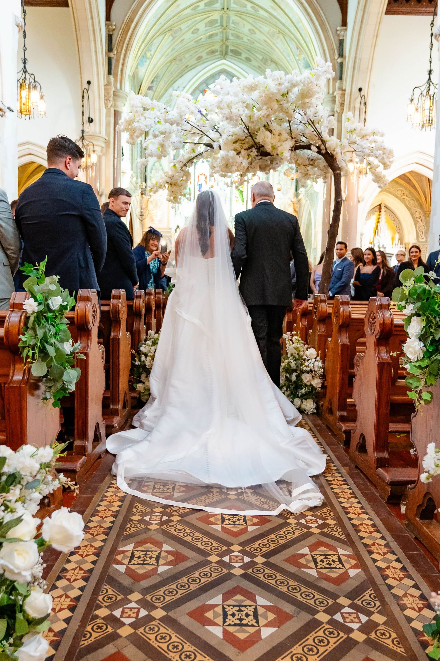 A panoramic view of a church wedding ceremony showing ornate floor tiles and elegant floral decorations along the aisle.