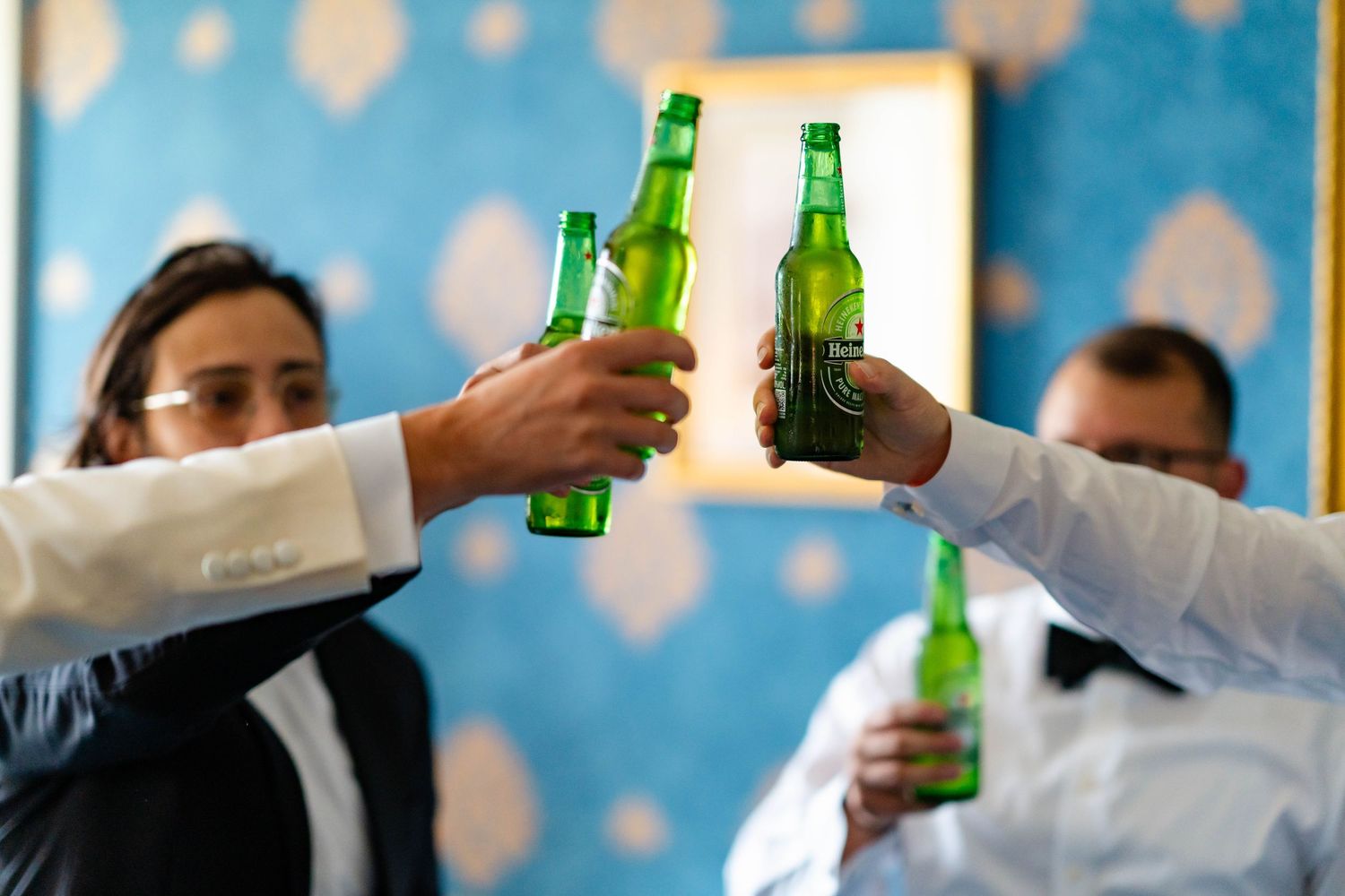 People raise beer bottles in a toast at a celebration with bokeh lights in the background.