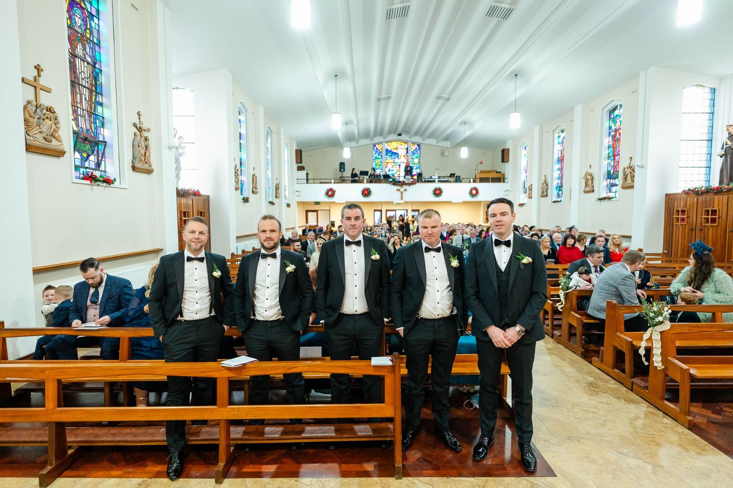 Wide angle view of church interior with wedding guests seated in wooden pews.