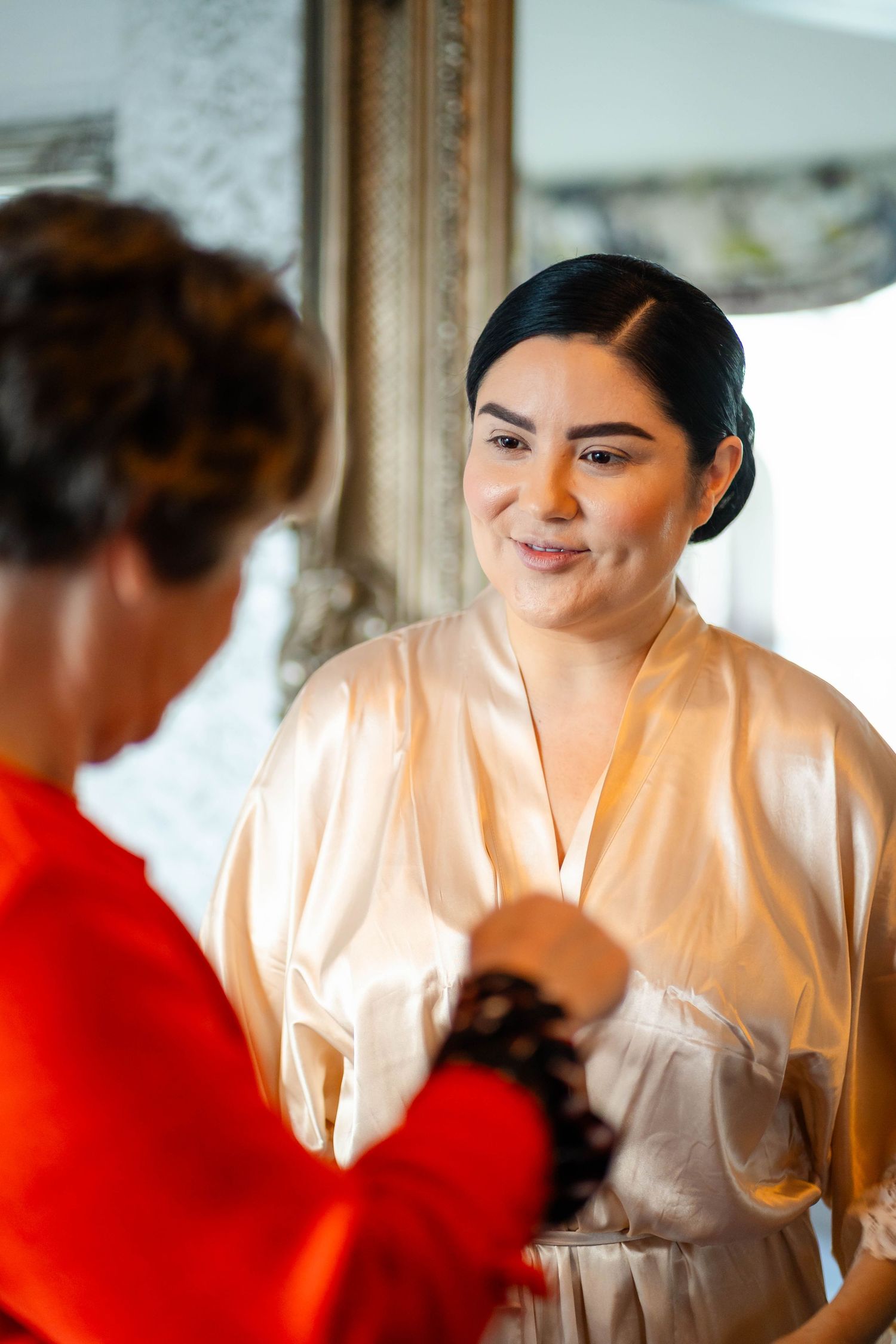 Person in white satin robe preparing for a special event with others in the background.